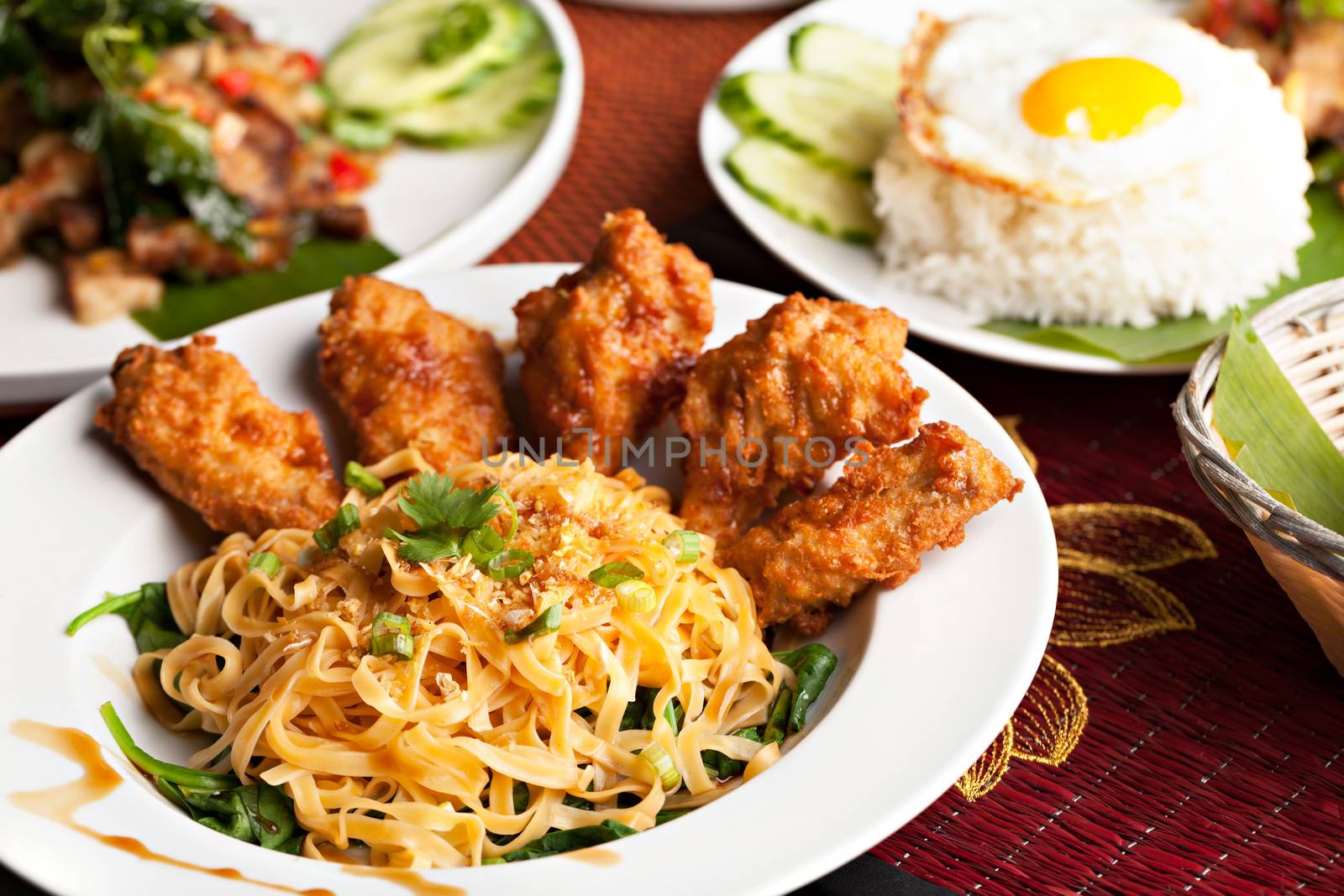 Thai style fried siracha chicken wings on a round white plate with egg noodles and spinach.