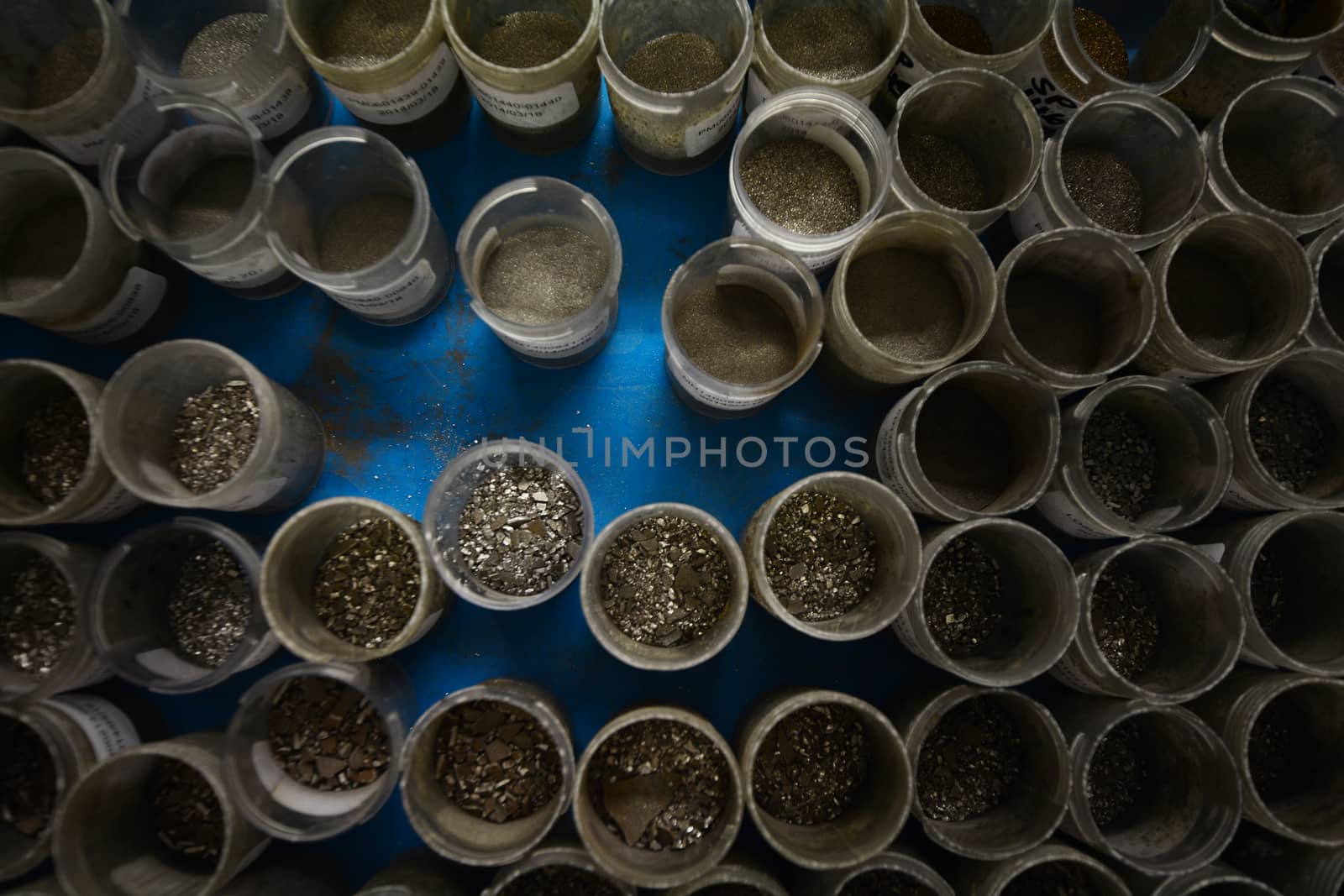 Top view of small plastic containers with various sized manganese flake grains. Blue background.