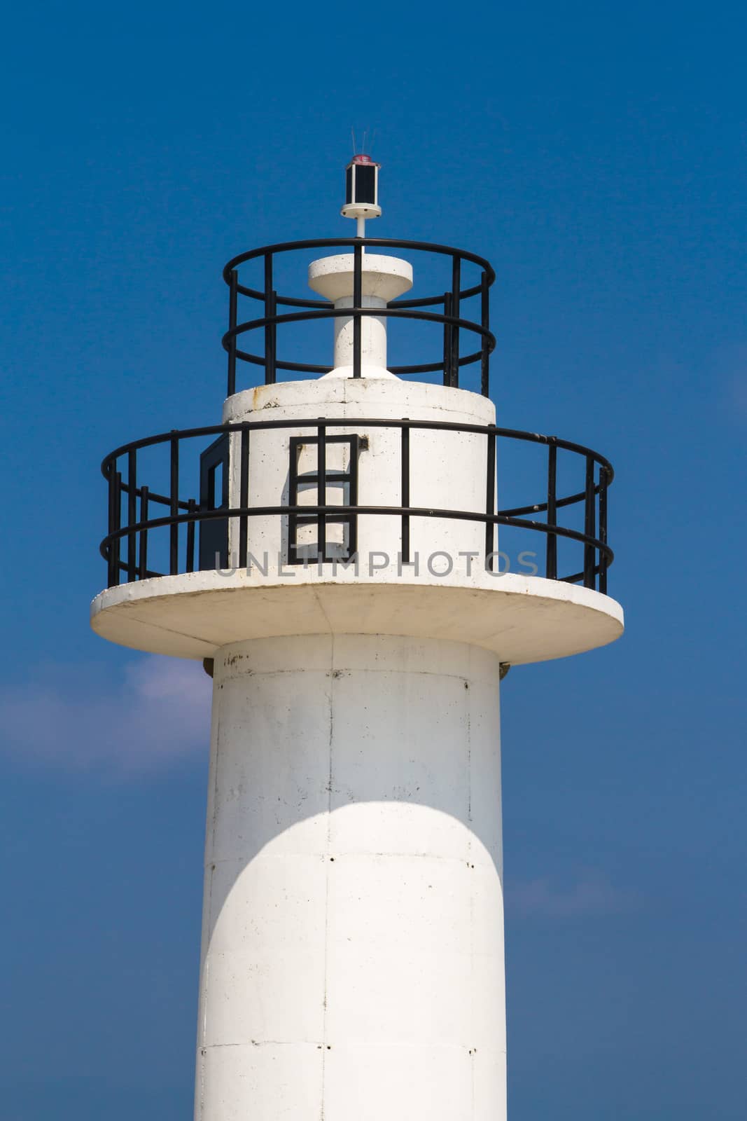 Close up view of white lighthouse on clear, blue sky.