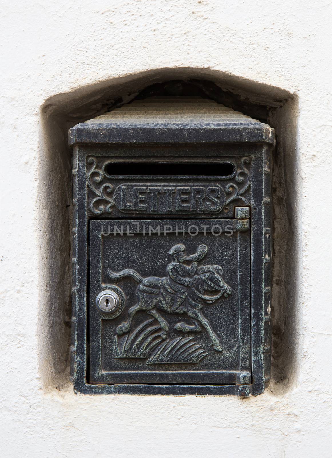 A black cast iron letterbox in a white wall niche with an engraving of a horse and knight and the word LETTERS.