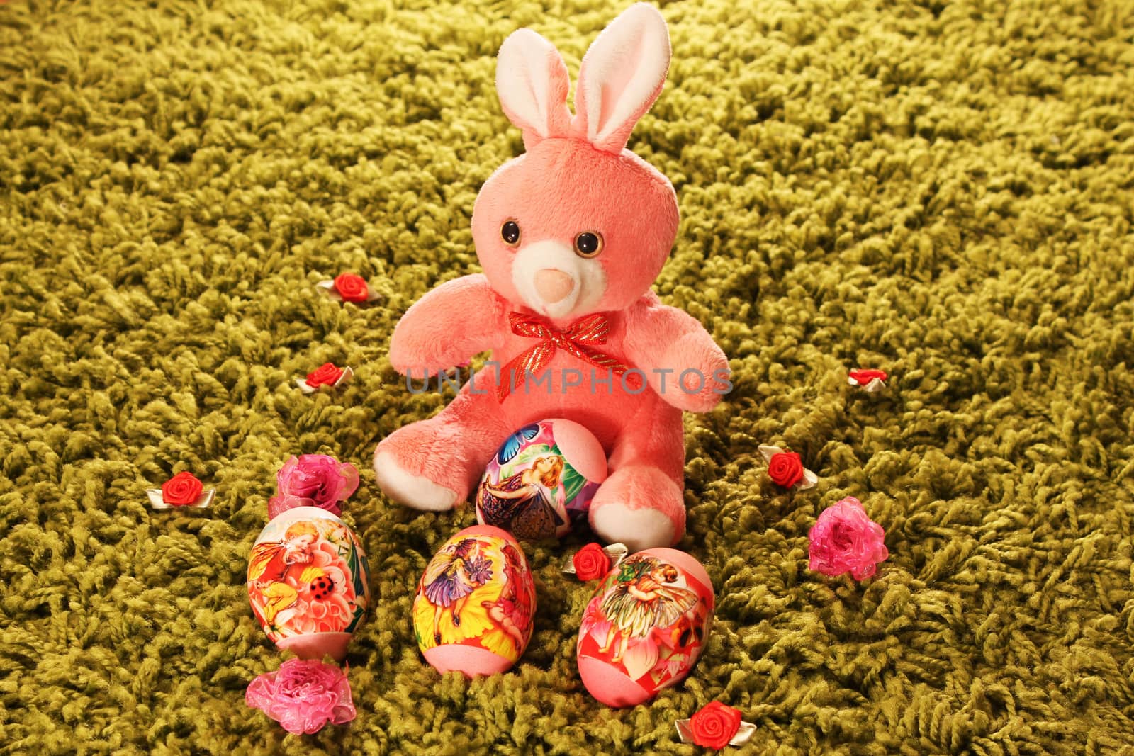 Easter eggs with pink toy rabbit placed on green synthetic grass with flowers