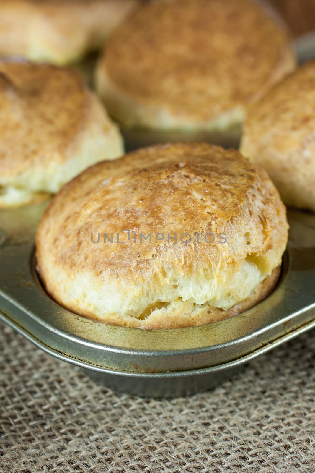 Fresh baked popovers in a metal muffin pan on a burlap surface.