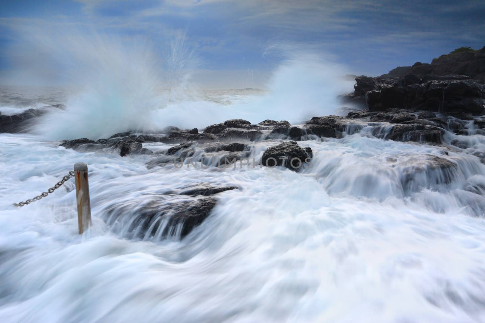 High tide and waves crashing onto the rocks bringing strong fast flowing water over the rocks and gushing past me into the rock pool at Kiama