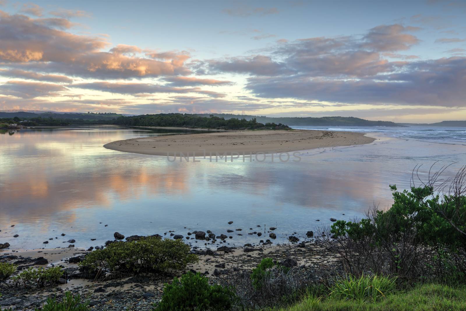 Picturesque sunrise as Minamurra river meets the ocean entrance and reflections in its waters.  South Coast NSW Austtralia.