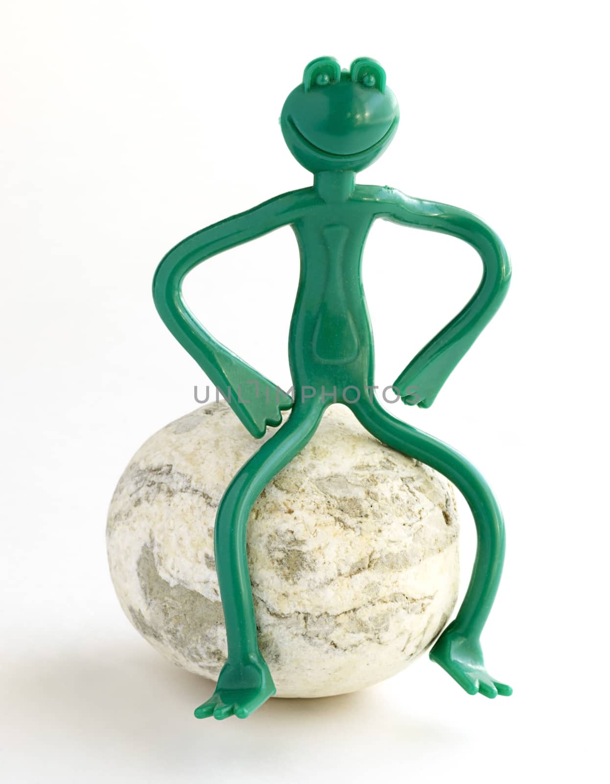 Green frog made of plastic sitting on the stone.