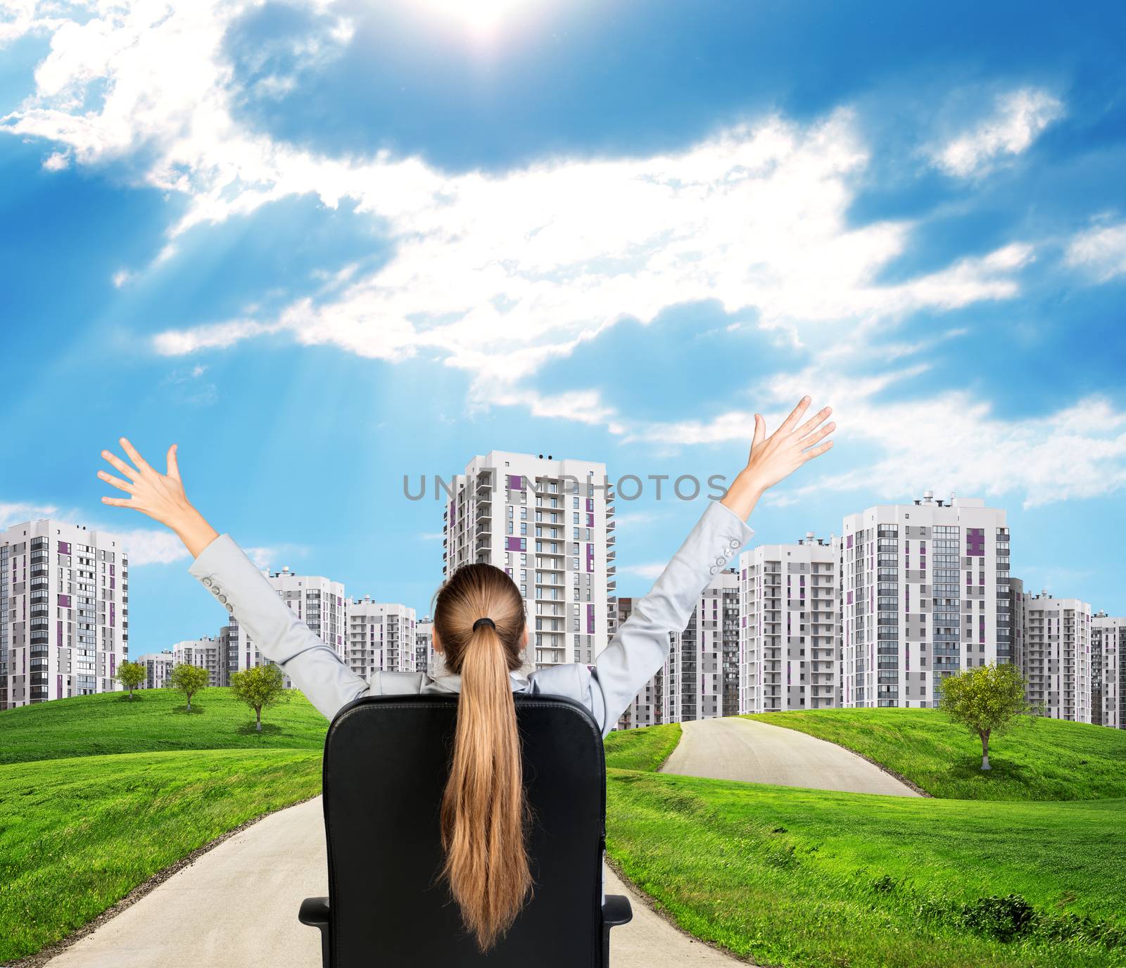 Businesswoman sitting on office chair with her hands outstretched. Green hills with buildings and sky as backdrop