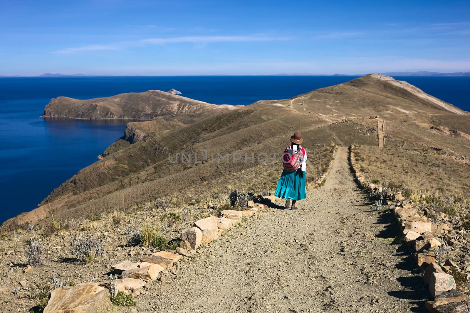ISLA DEL SOL, LAKE TITICACA, BOLIVIA - NOVEMBER 7, 2014: Unidentified woman in traditional wear walking on path on November 7, 2014 on Isla del Sol, Lake Titicaca, Bolivia. Isla del Sol (Island of the Sun) is a popular travel destination. 