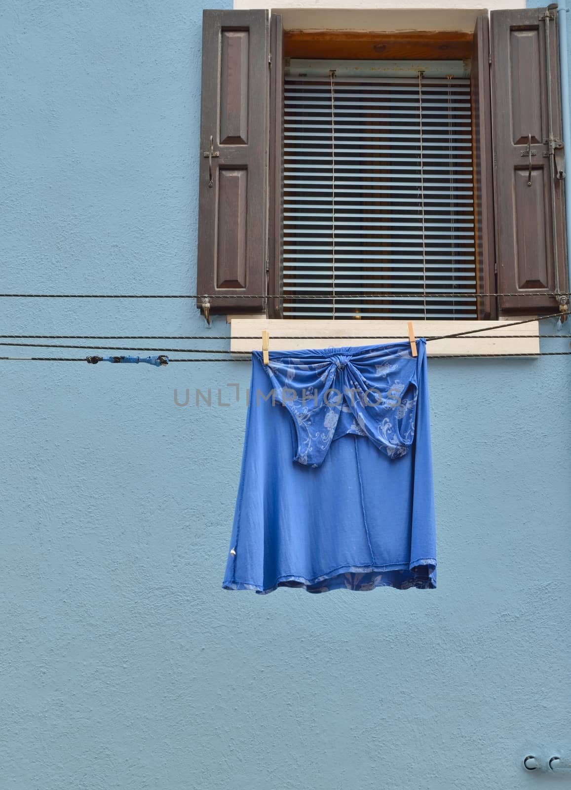 Blue dress hanging on blue facade  of a house of Burano, small fisher village in Venice lagoon.