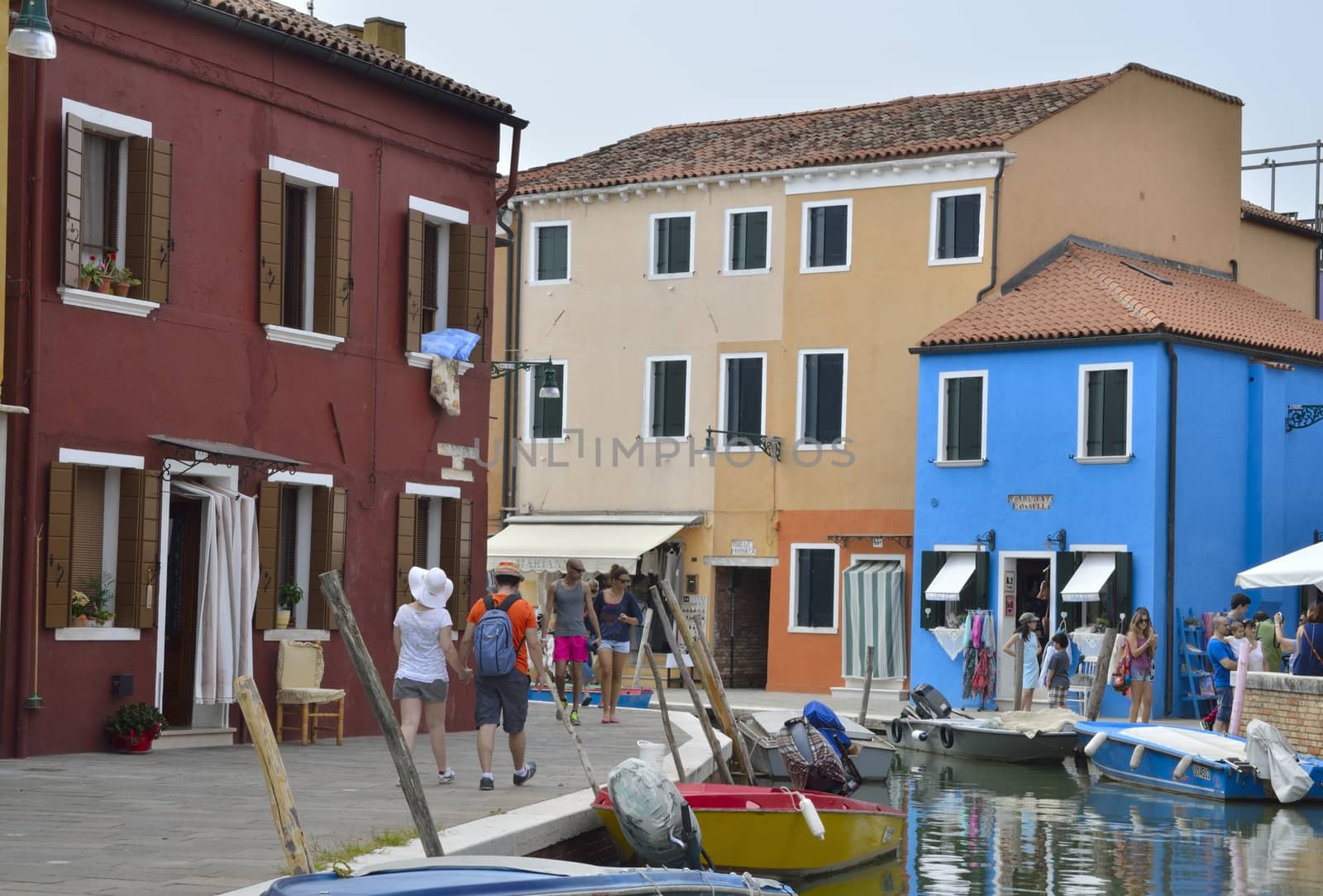 Tourists walking by a way along a small canal in Burano, a colorful island of Venice, Italy