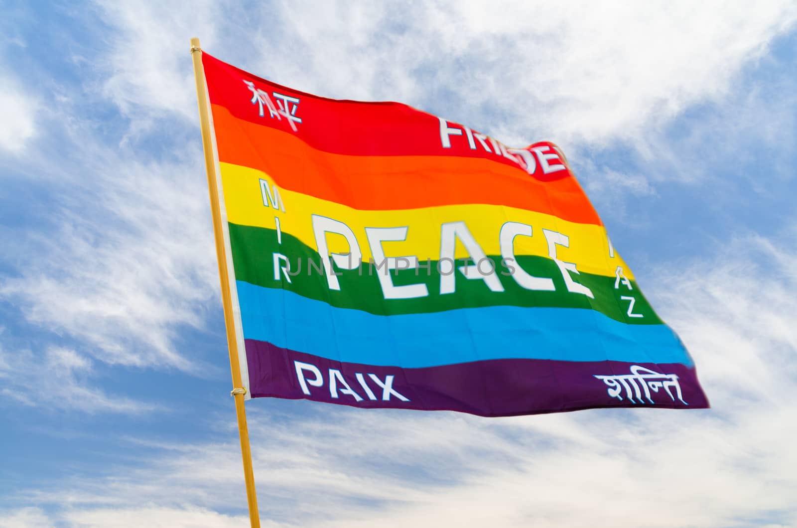 Waving rainbow varicolored peace flag with multilingual pacific text flying on wind against blue sky