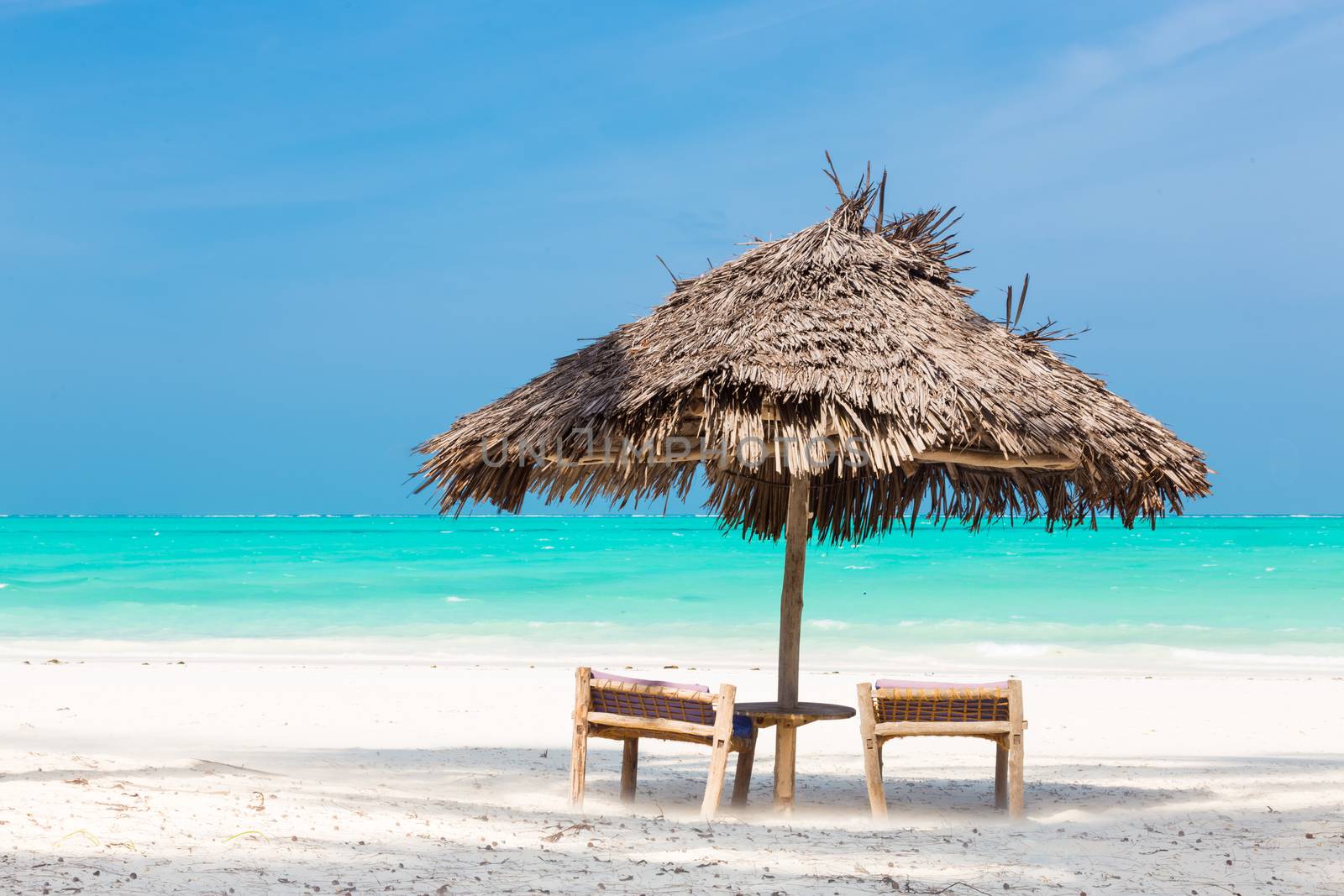 Two wooden dack chairs and umbrella on stunning tropical beach. Turquoise blue lagoon of Paje beach, Zanzibar, Tanzania.