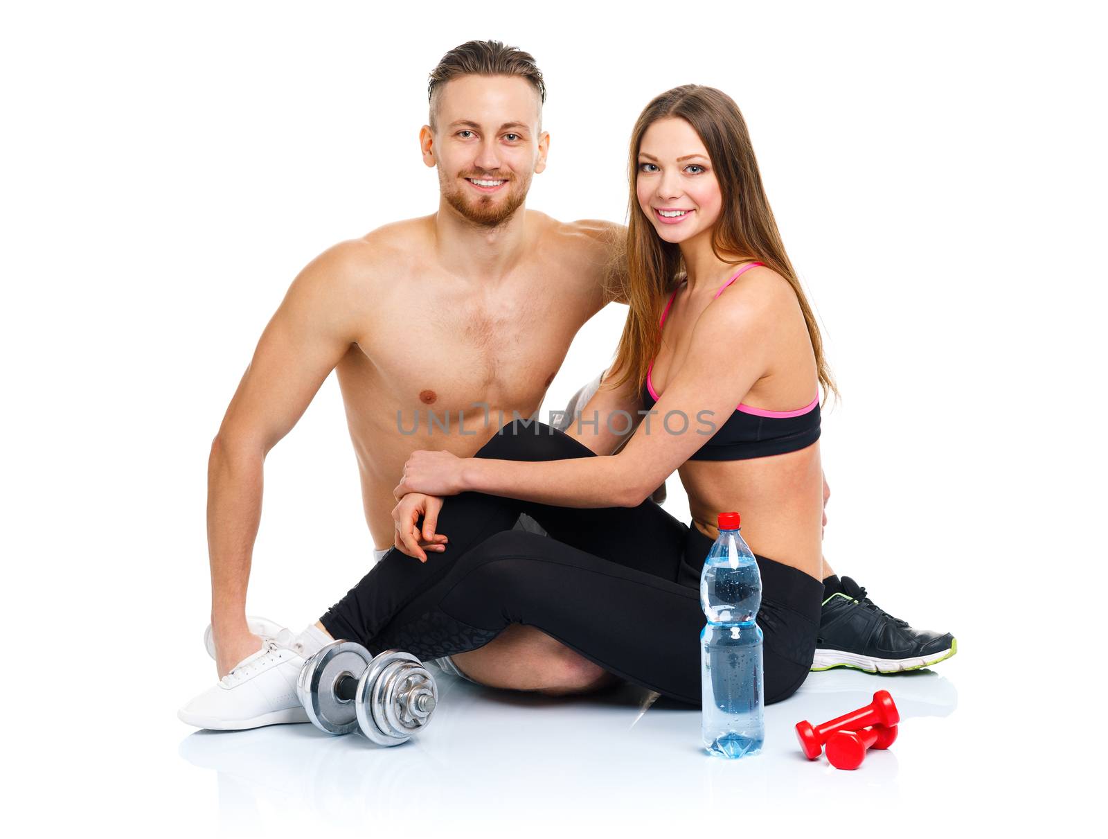 Athletic couple - man and woman after fitness exercise with dumbbells and bottle of water sitting on the white background
