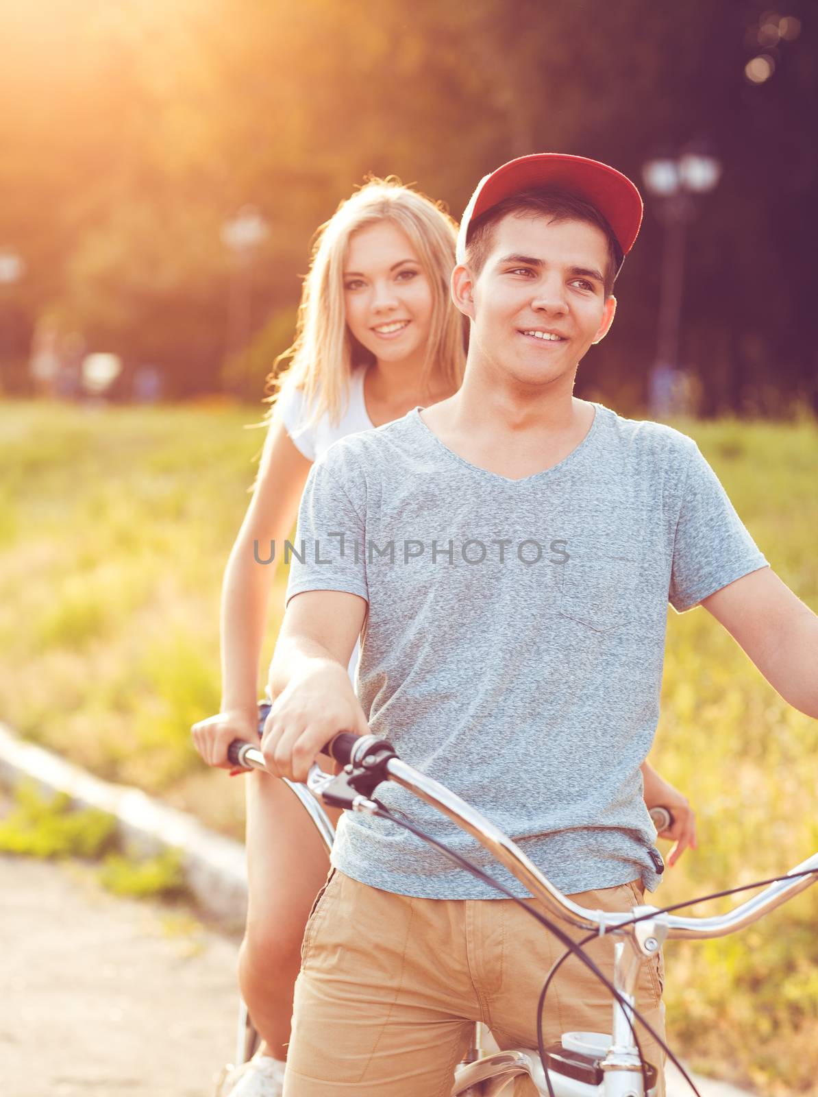 Happy couple - young man and woman riding a bicycle in the park outdoors