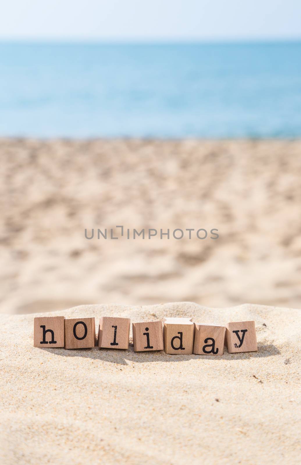 Holiday word on wood rubber stamps stack on the sand beach for vacation and summer season concept, beautiful sea view during daytime on a sunny day with blue sky on background