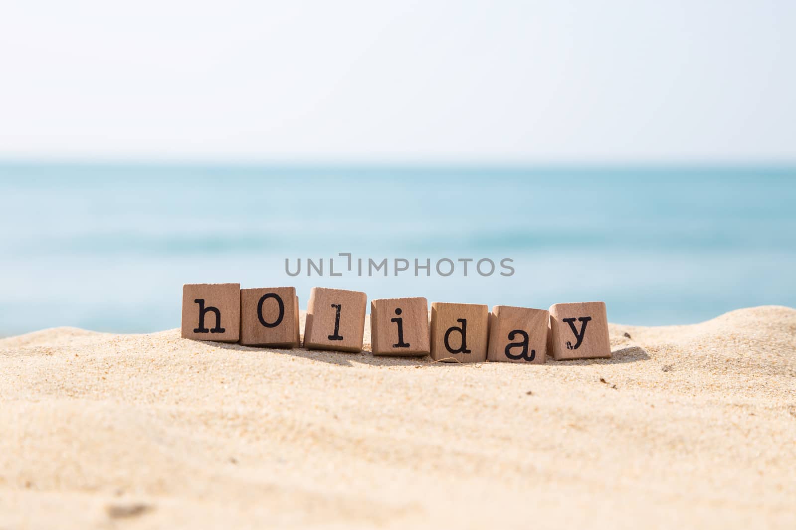 Holiday word on wood rubber stamps stack on the sand beach for vacation and summer season concept, beautiful ocean view during daytime on a sunny day with blue sky on background