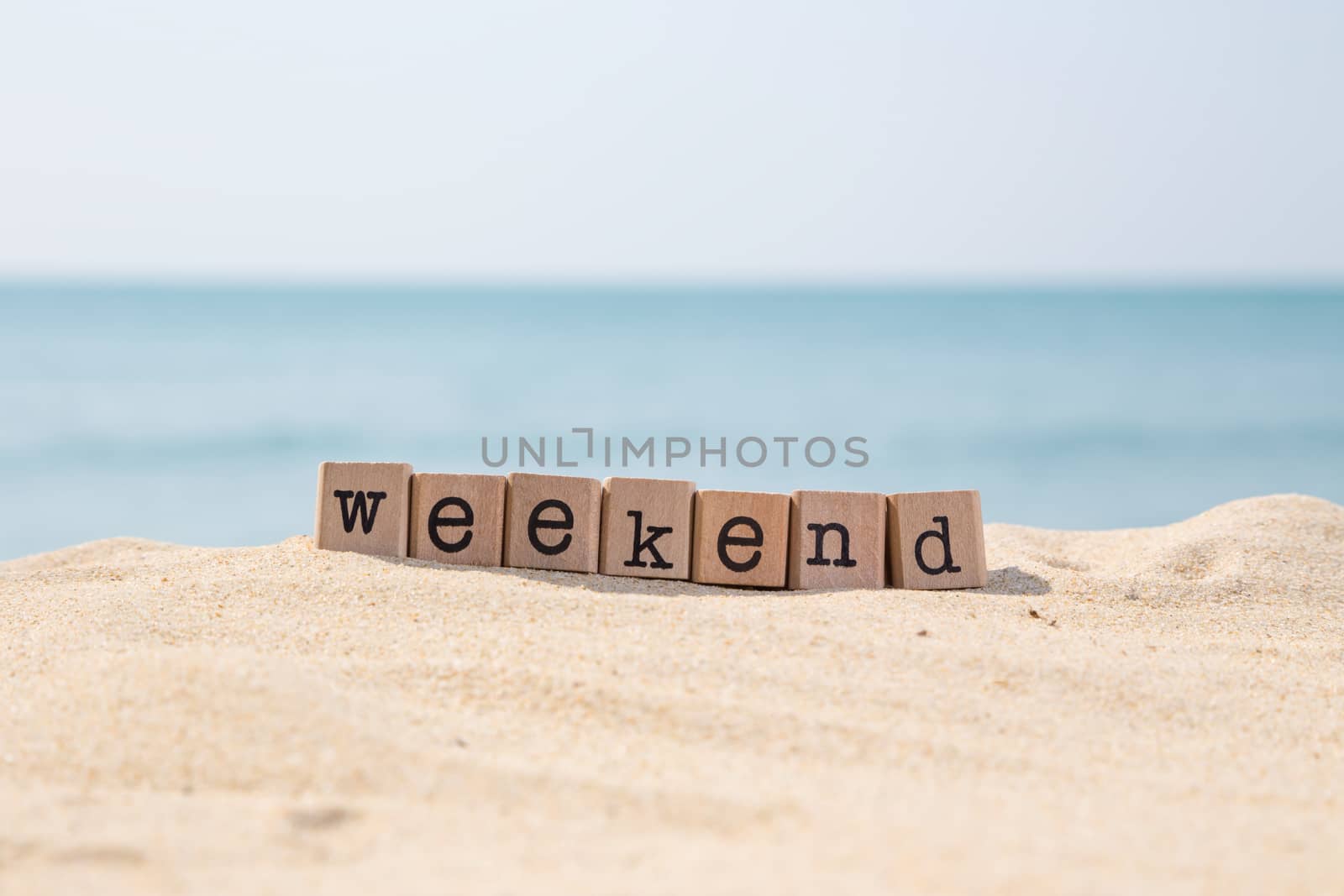 Weekend word on wood rubber stamps stack on the sand beach for vacation and summer season concept, beautiful ocean view during daytime on a sunny day with blue sky on background
