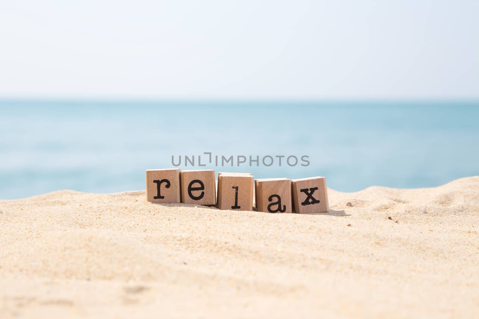 Relax word on wood rubber stamps stack on the sand beach for break and vacation concept, beautiful ocean view during daytime on a sunny day with blue sky on background