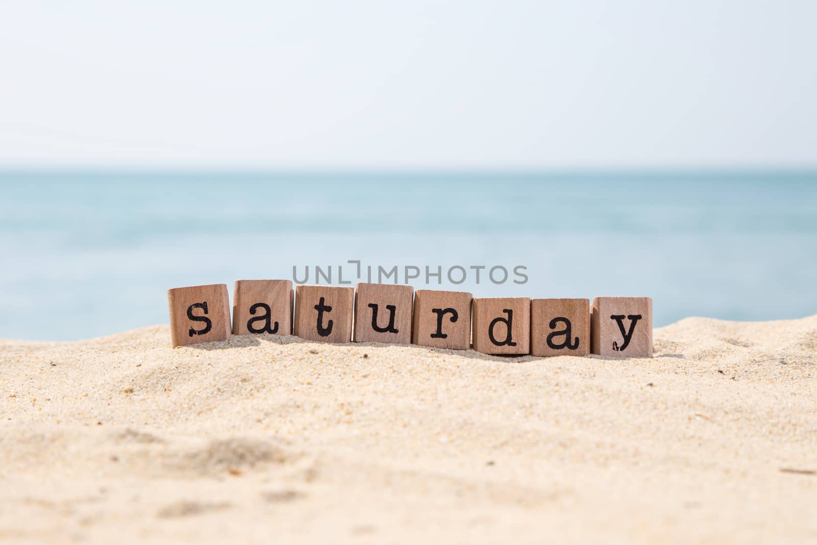 Saturday word on wood rubber stamps stack on seaside with beautiful blue sea view on background, day and time concepts