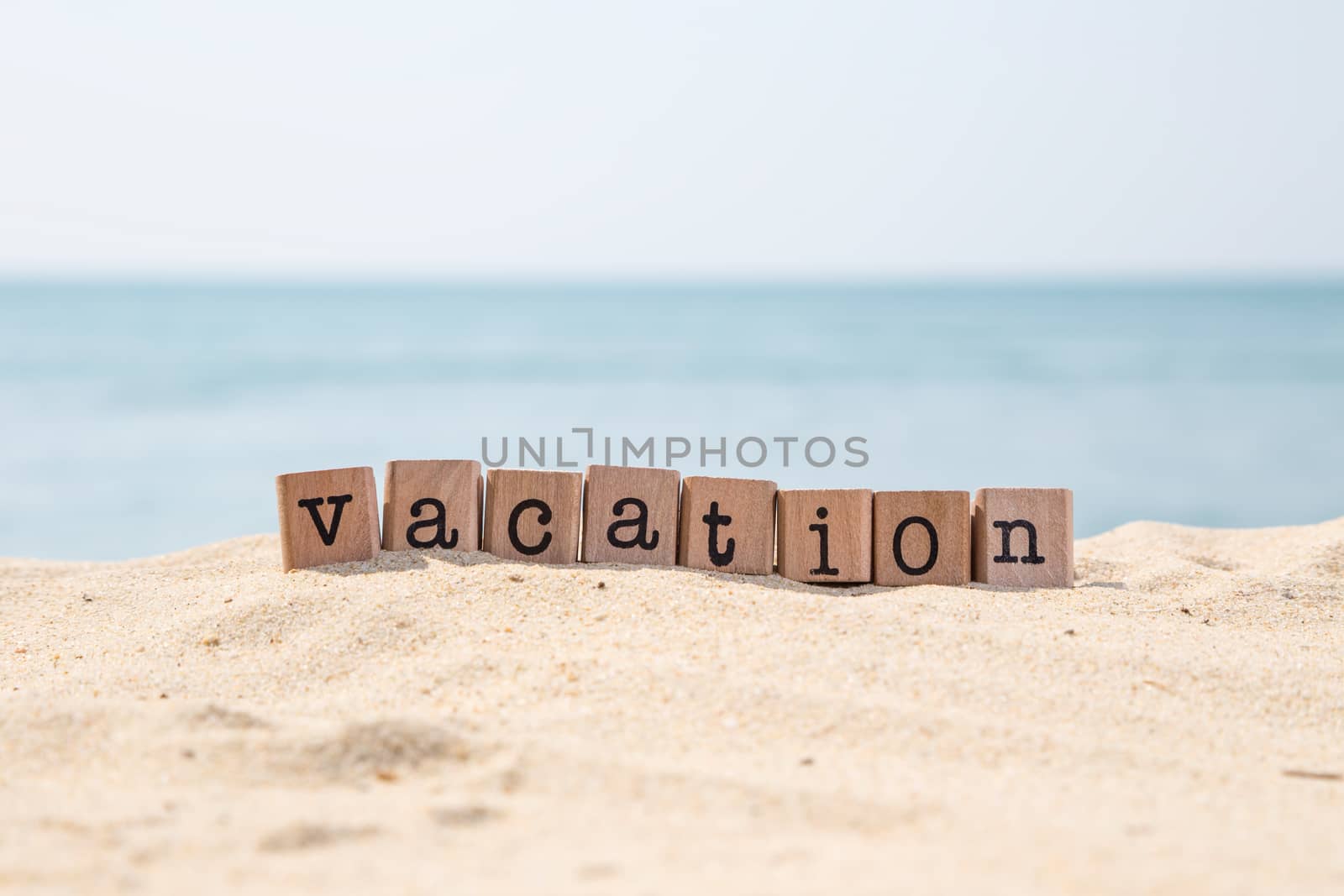 Vacation word on wood rubber stamps stack on the sand beach for holiday and summer season concepts, beautiful blue ocean view during daytime on a sunny day on background