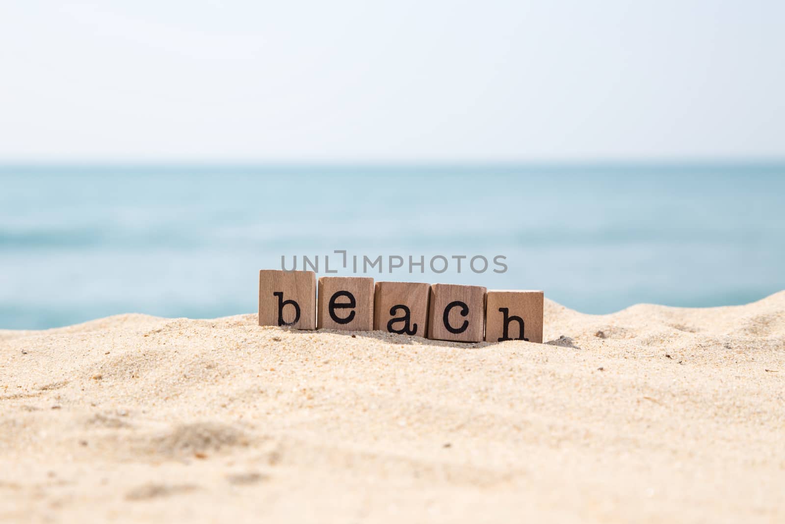 Beach word on wood rubber stamps stack on seaside for vacation and summer season concepts, beautiful blue ocean view during daytime on a sunny day on background