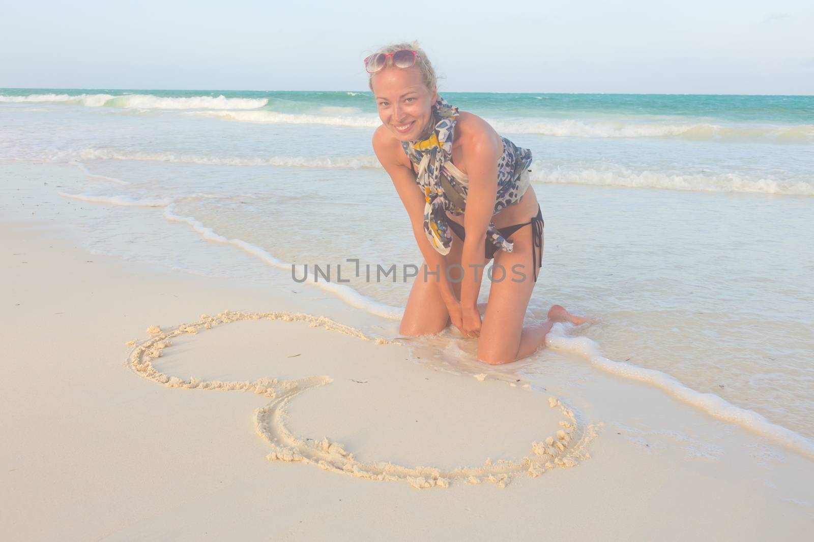 Beautiful woman drawing a heart in the sand on the beach.