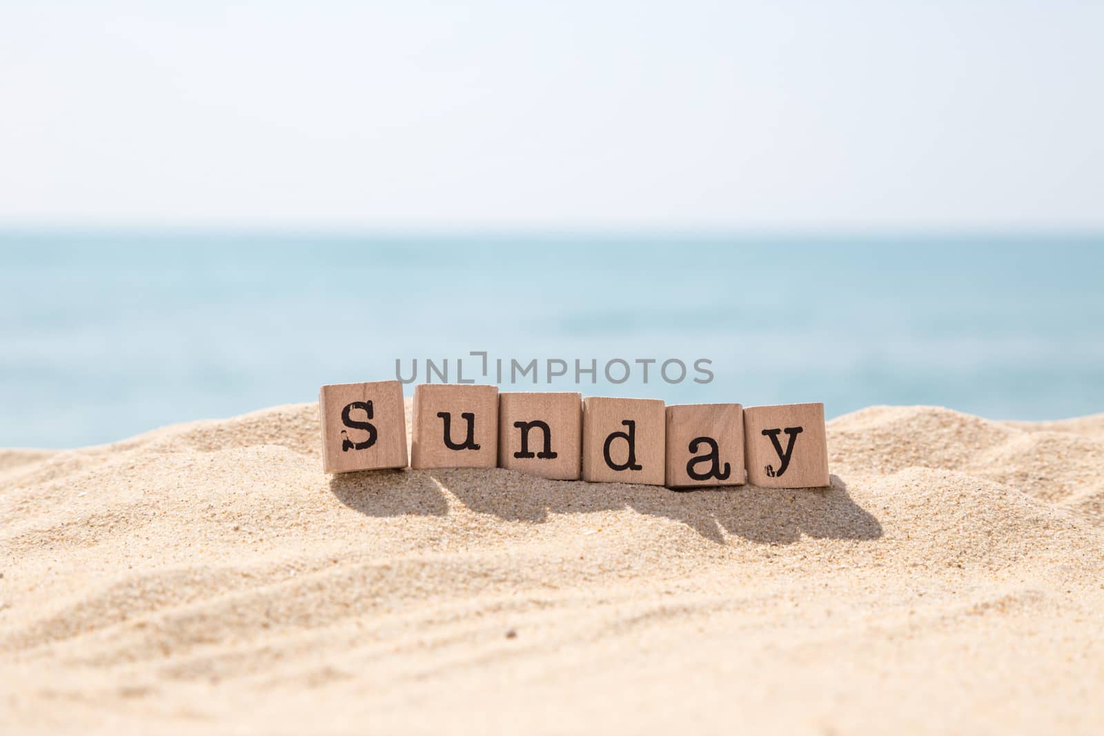 Sunday word on wood rubber stamps stack on beach with beautiful blue sea view on background, day and time concepts