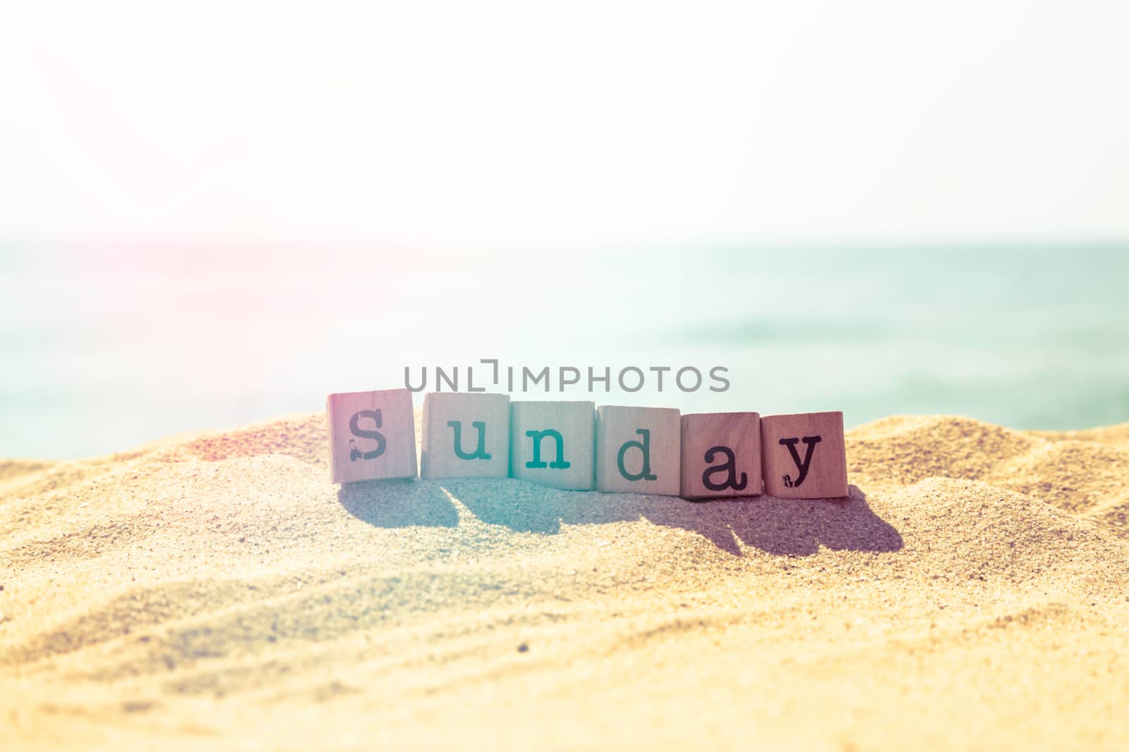 Sunday word on wood rubber stamps stack on sunny beach with beautiful sea view on background, retro style image with light leak