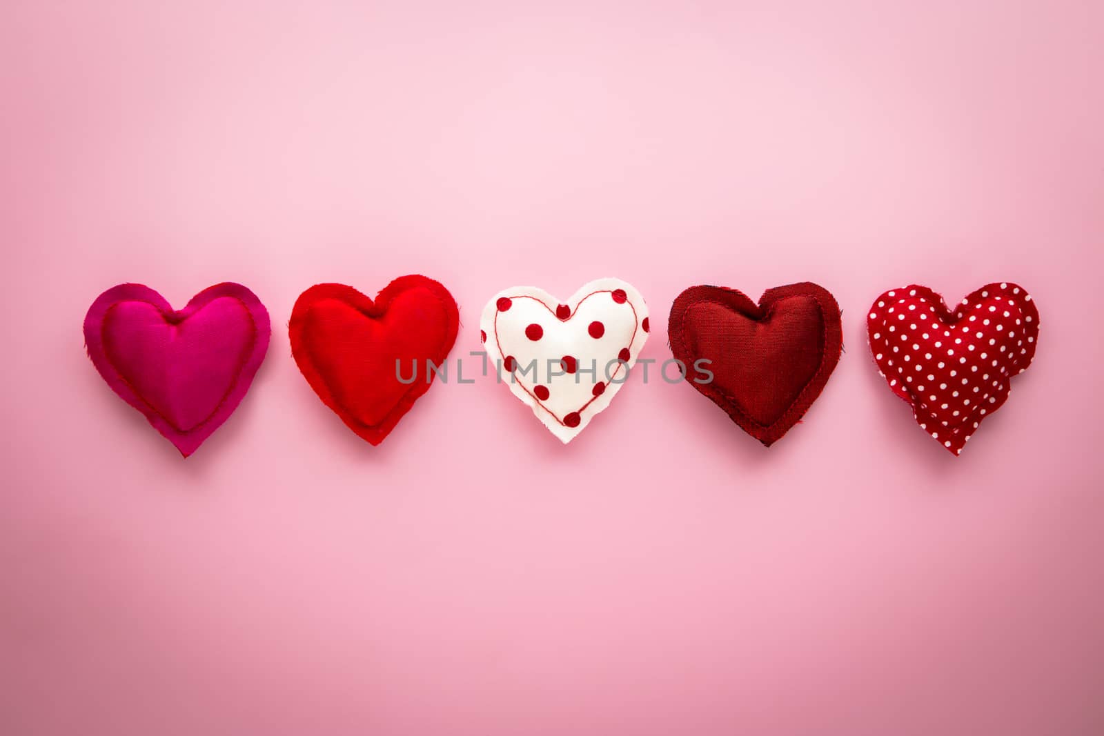 Group of sweet hearts handmade crafts from red tone silk and cotton cloths place on pink paper background with vignette, love and valentine's day symbol