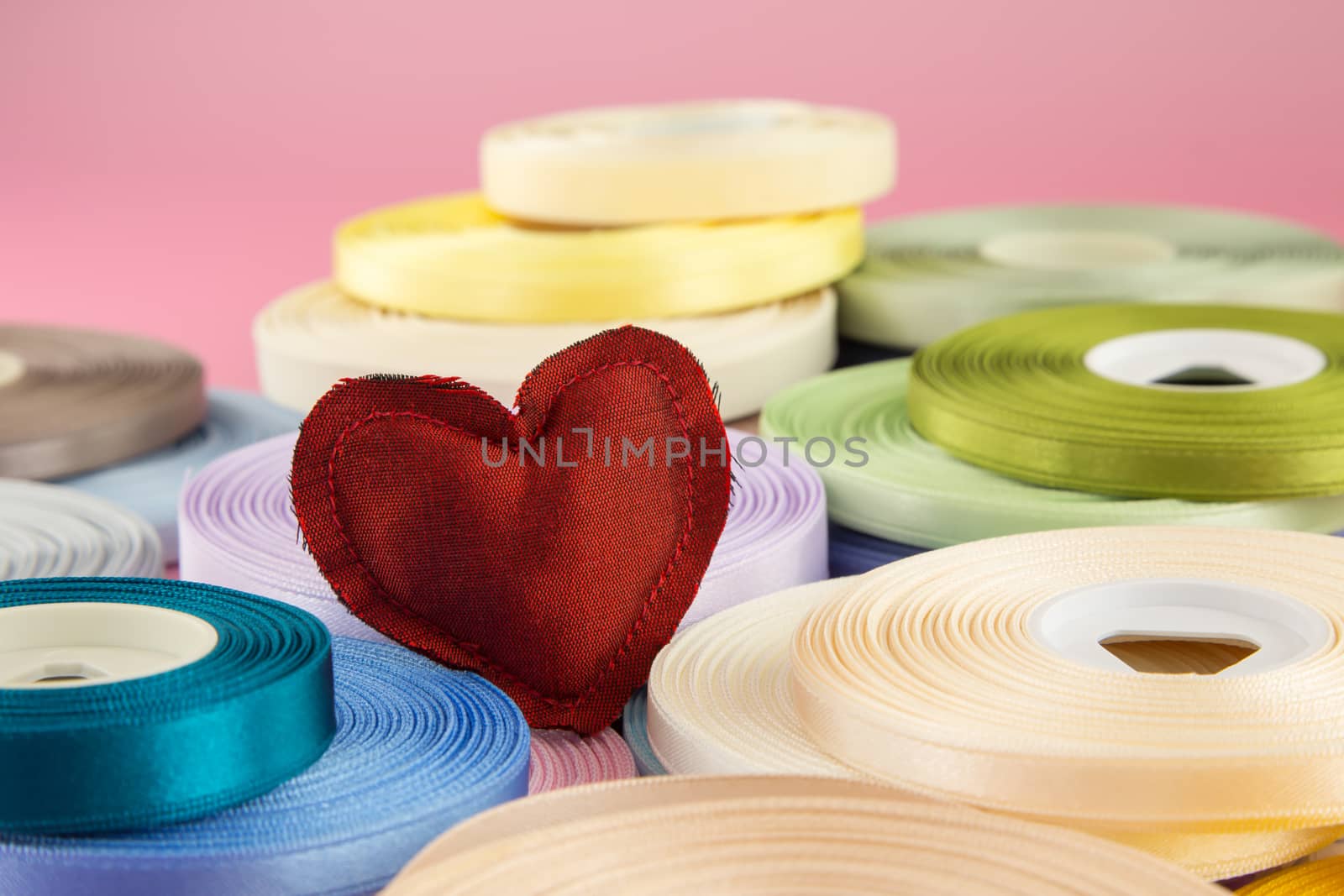 Red heart handmade craft from silk cloth stack on ribbon rolls, love and valentine's day symbol