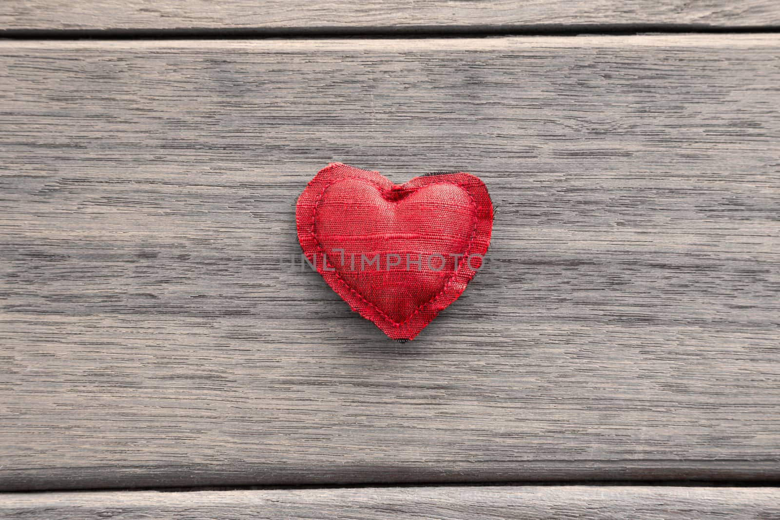 Red heart handmade craft from silk cloth place in the middle of wood background, valentine's day symbol