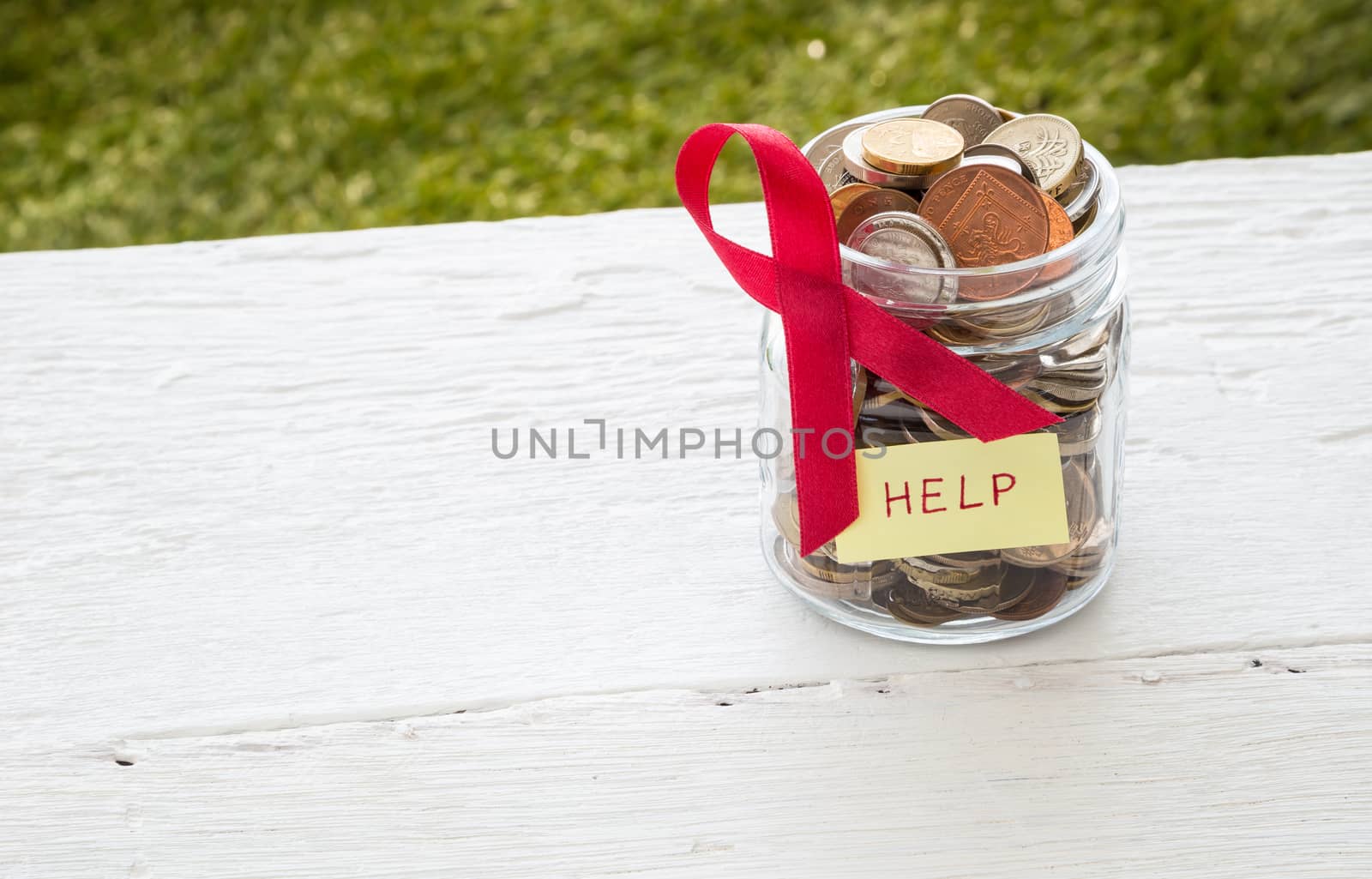 World coins in money glass jar with HELP word label and breast cancer ribbon sign place on white wood table, donation and charity concept