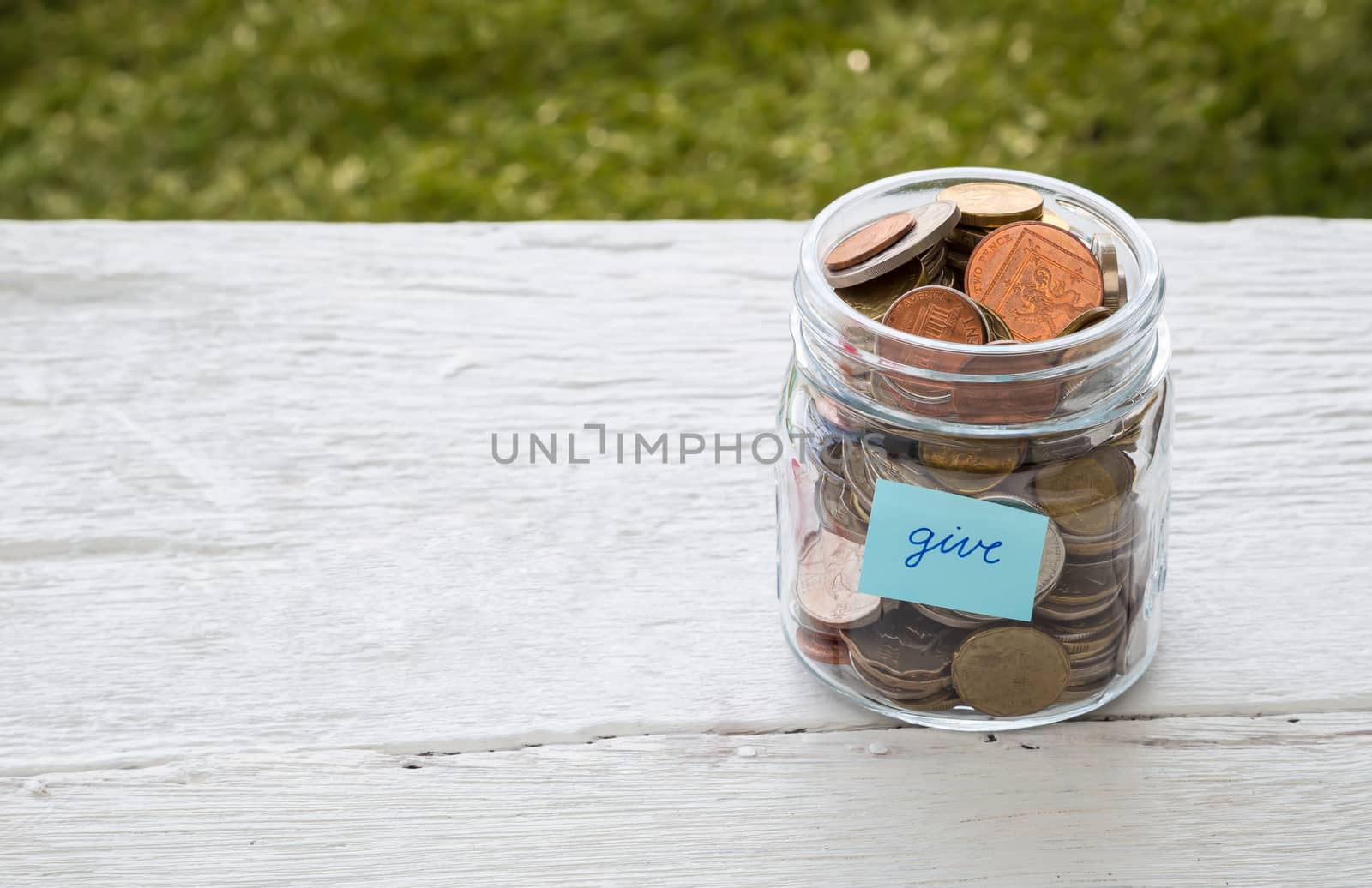 World coins in money glass jar with blue GIVE word label place on white wood table, blank space for text,  donation and charity concept