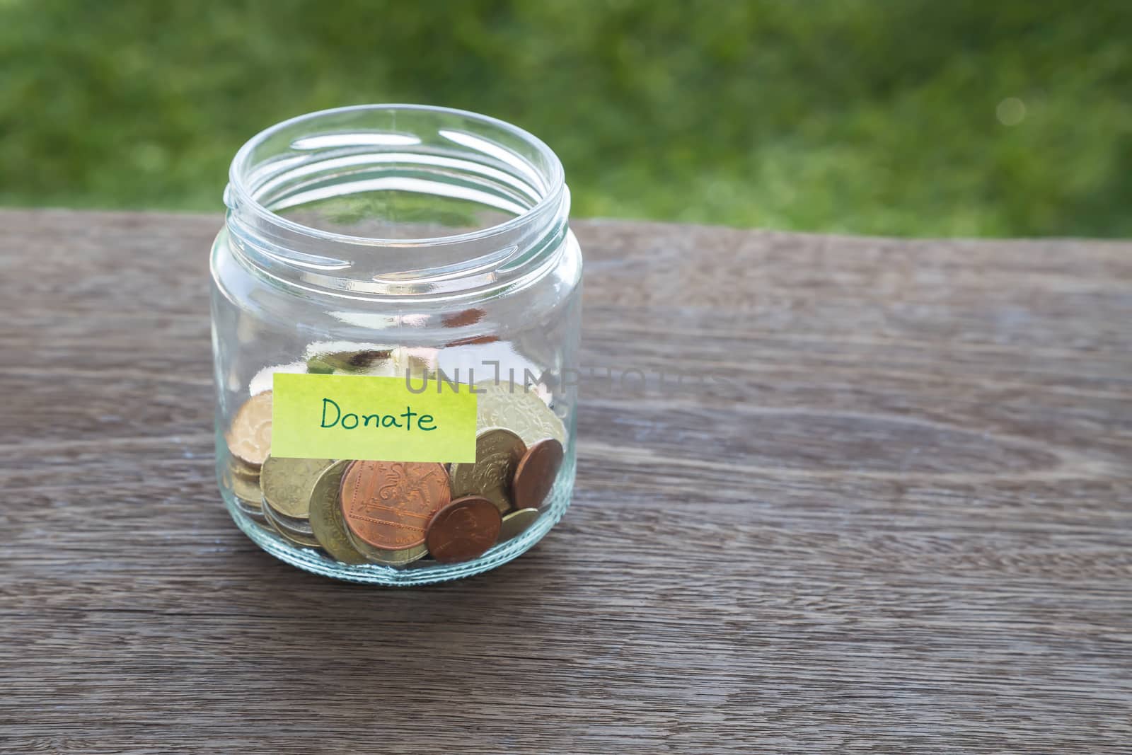 World coins in money glass jar with DONATE word label place on natural wood table, blank space for text