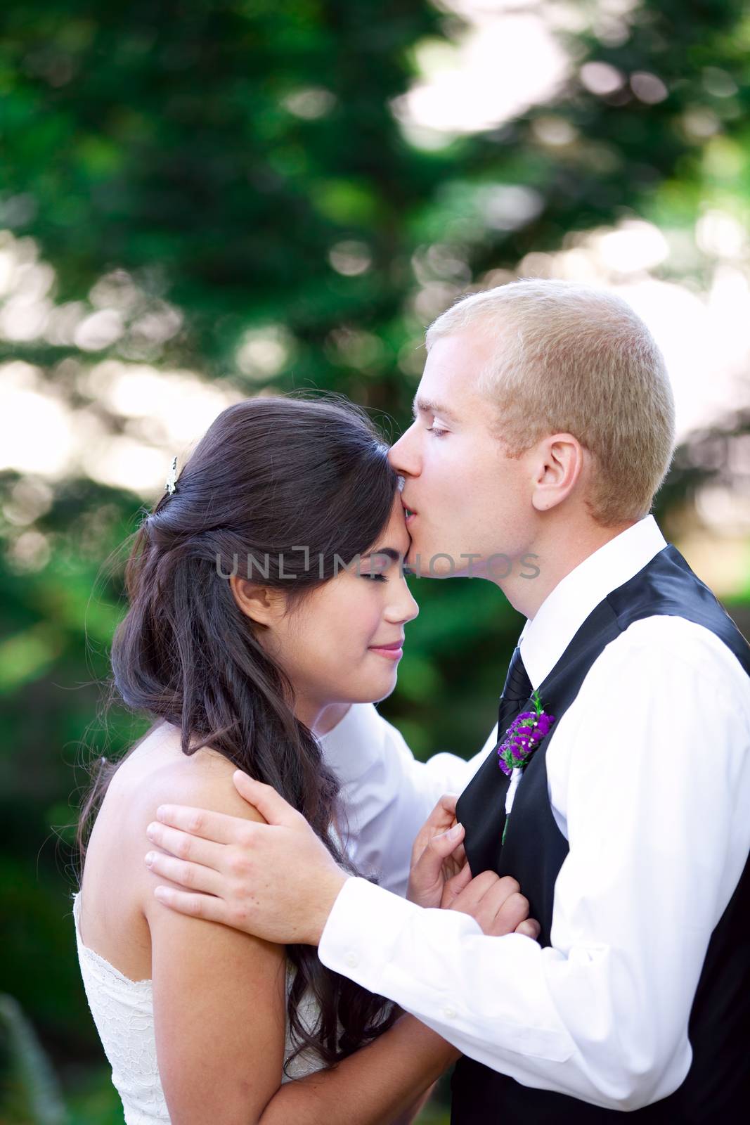 Caucasian groom lovingly kissing his biracial bride on cheek. Diverse couple