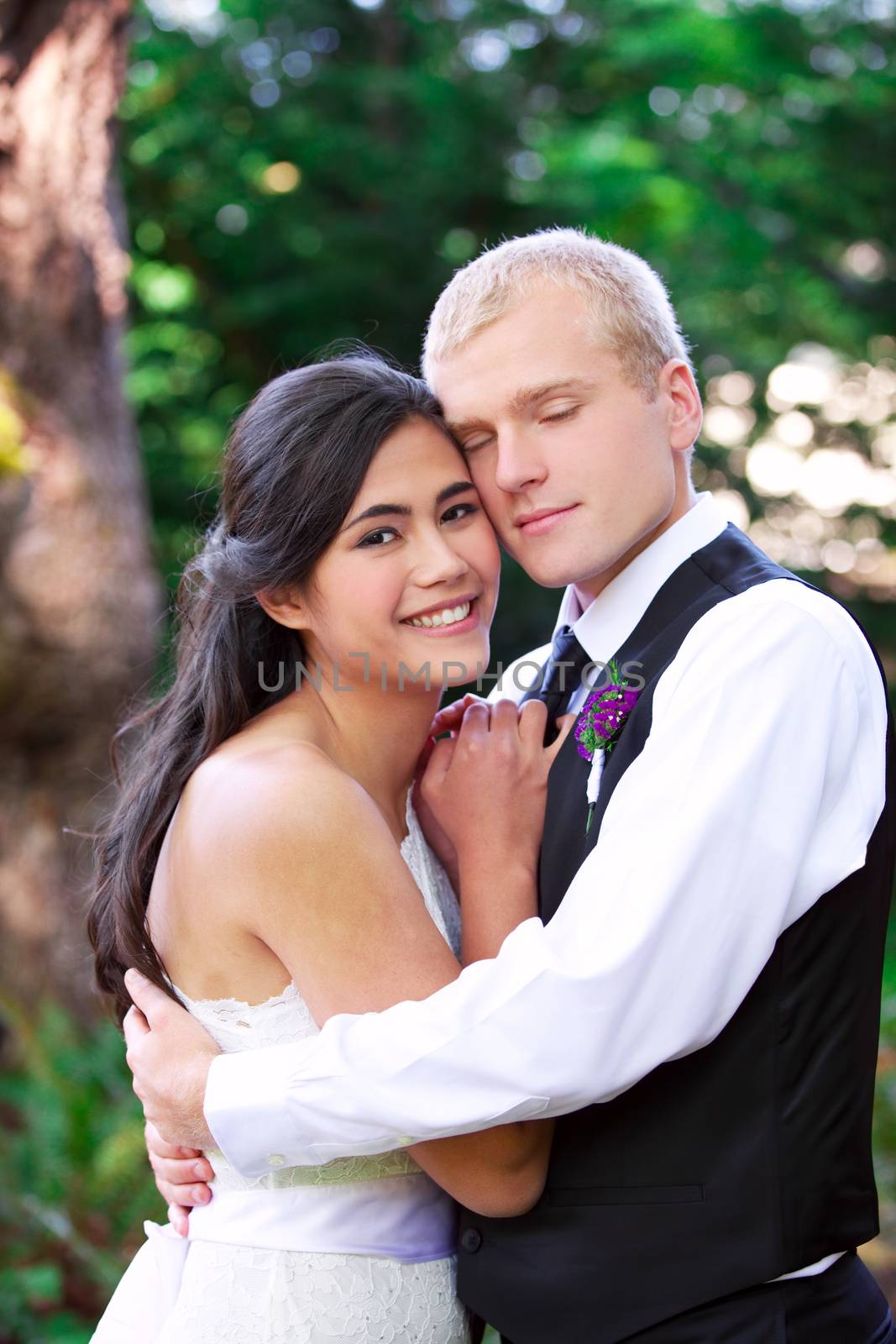 Caucasian groom holding his biracial bride, smiling. Diverse couple.