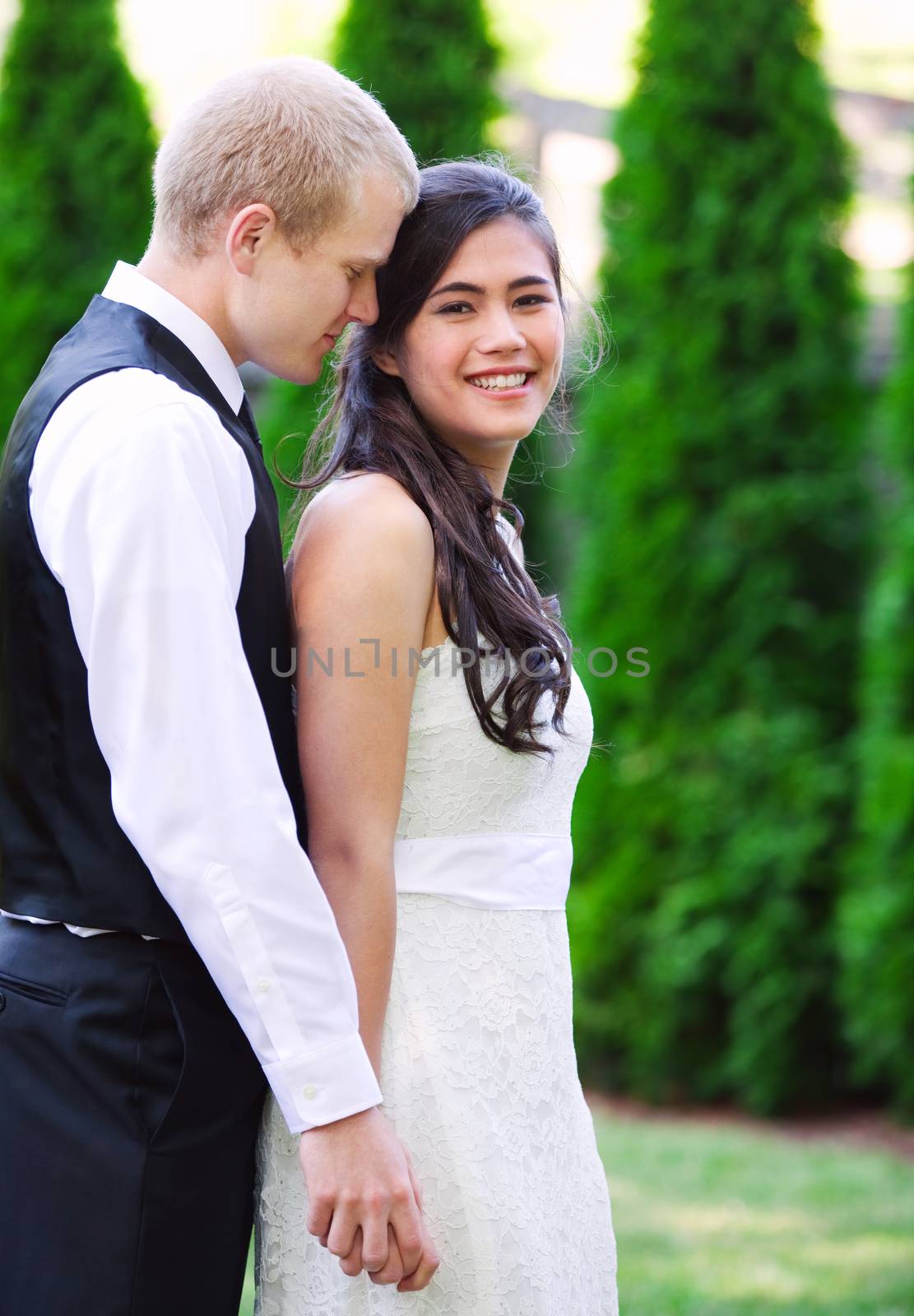 Caucasian groom holding his biracial bride, smiling. Diverse couple.