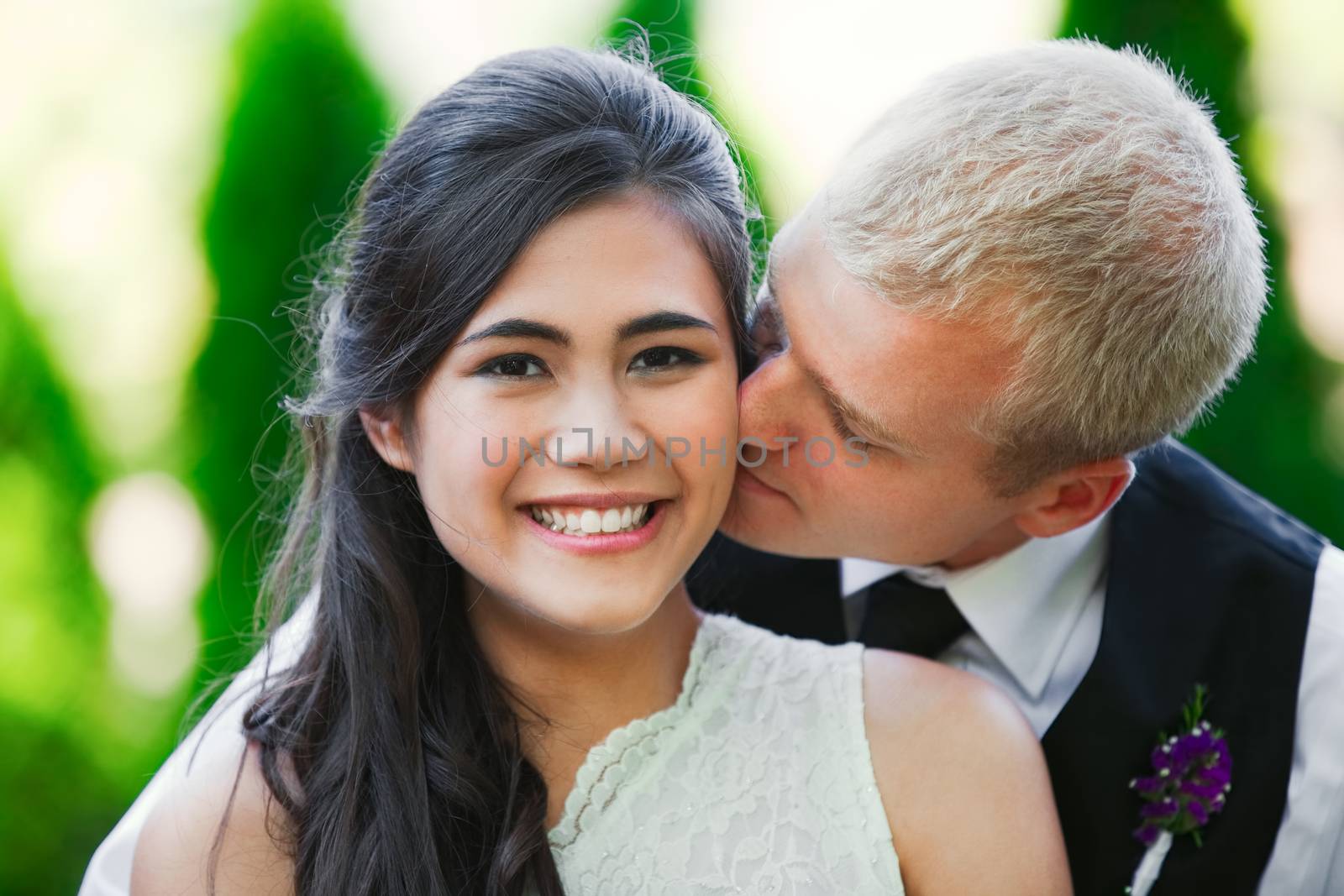 Caucasian groom lovingly kissing his biracial bride on cheek. Di by jarenwicklund