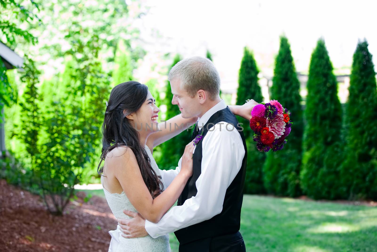 Caucasian groom holding his biracial bride, smiling. Diverse cou by jarenwicklund