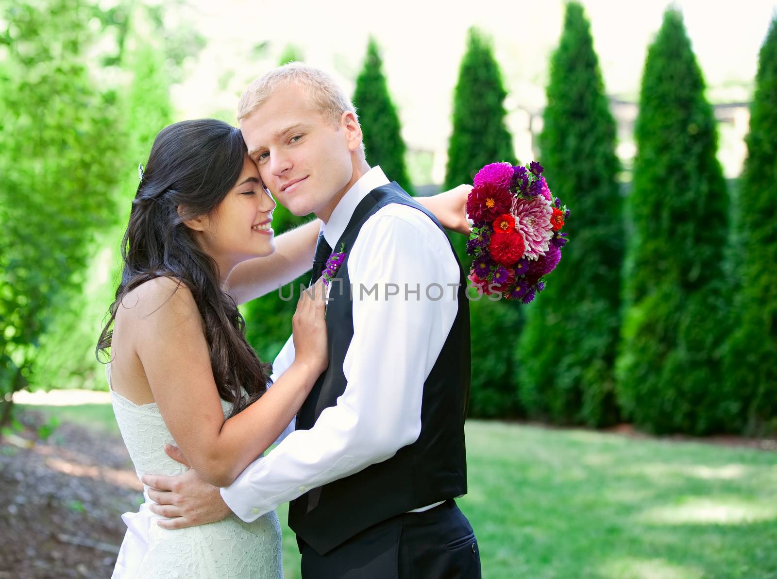 Caucasian groom holding his biracial bride, smiling. Diverse couple.