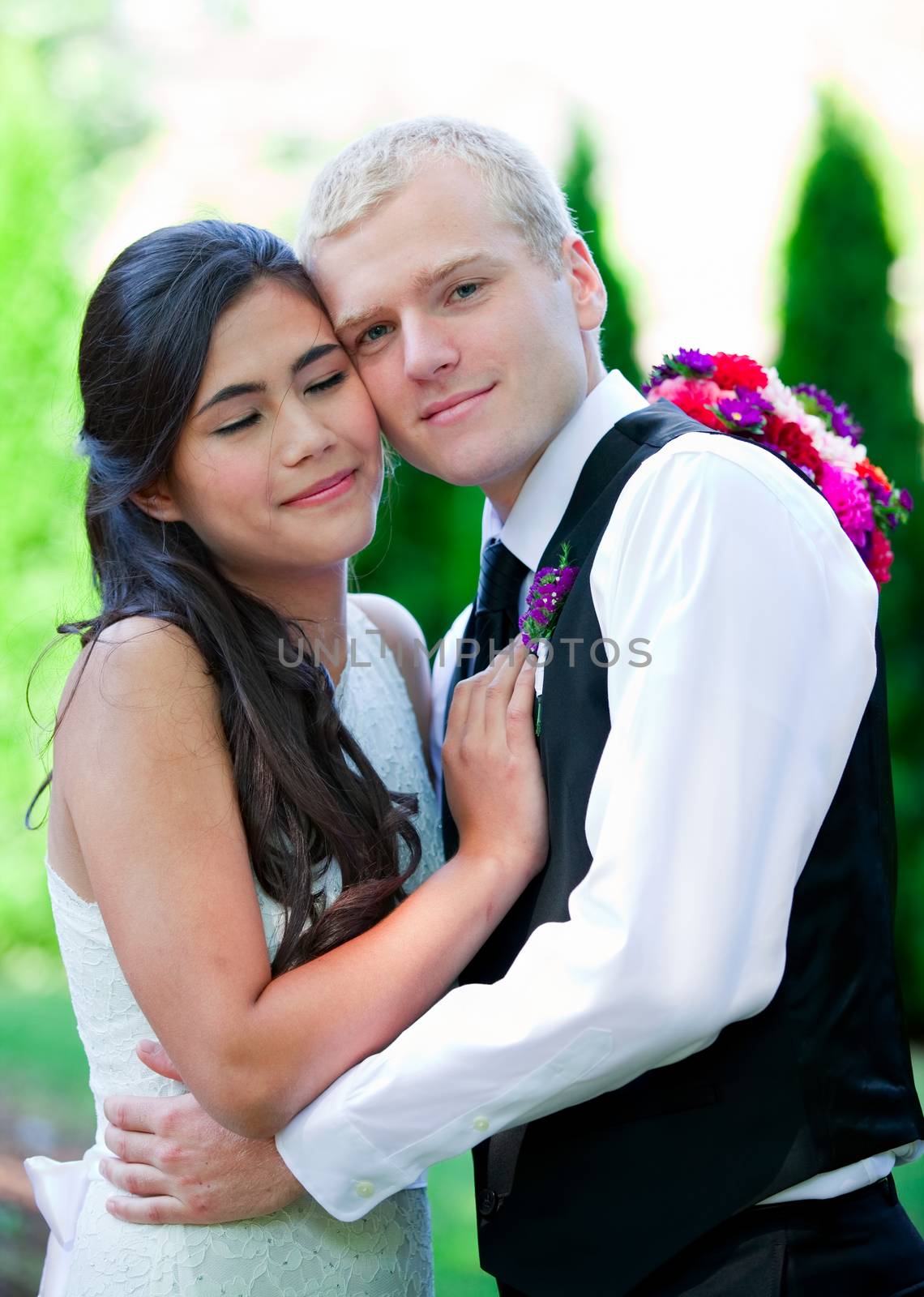 Caucasian groom holding his biracial bride, smiling. Diverse couple.