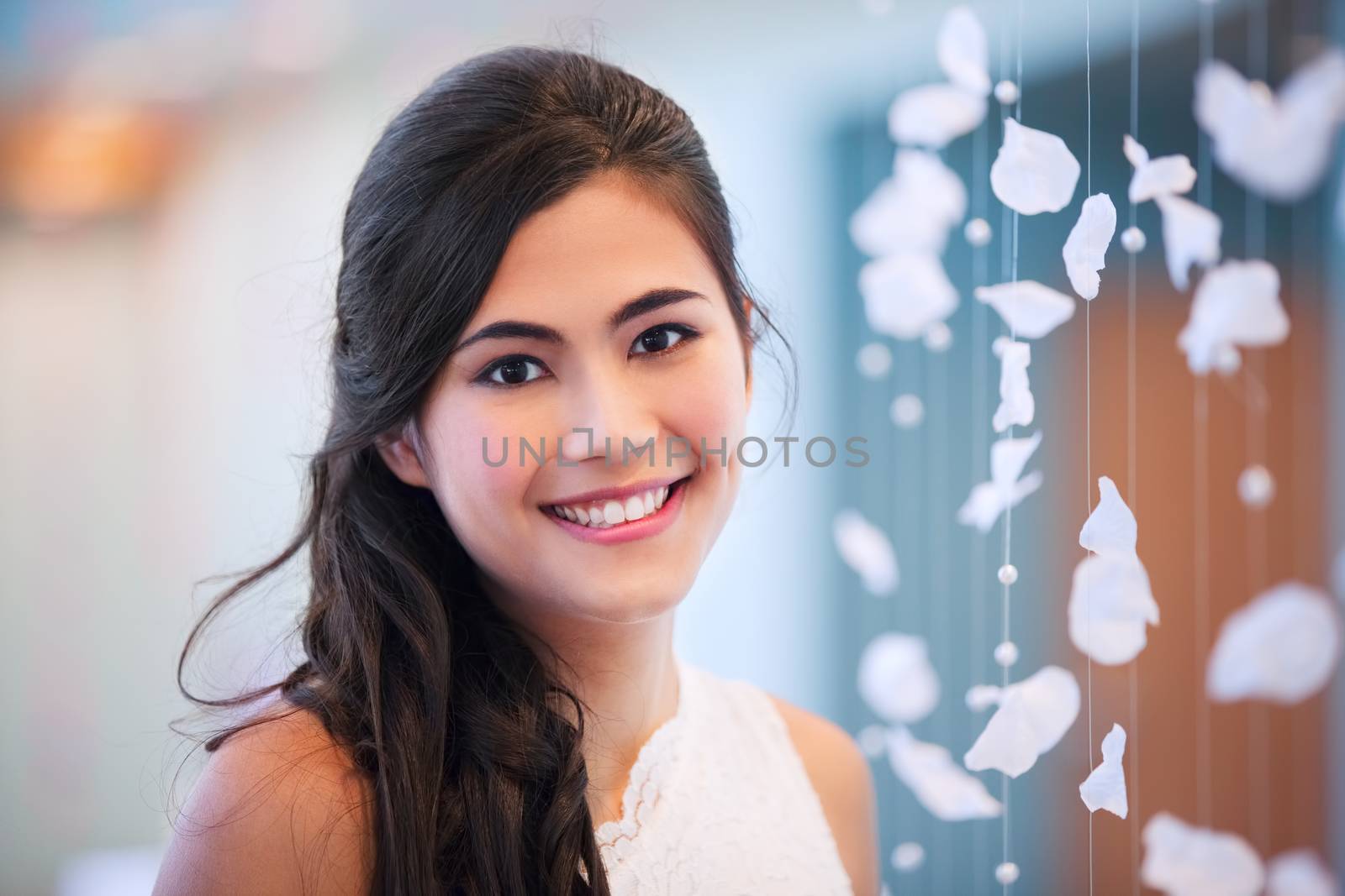 Beautiful biracial bride smiling next to curtain of white rose petals
