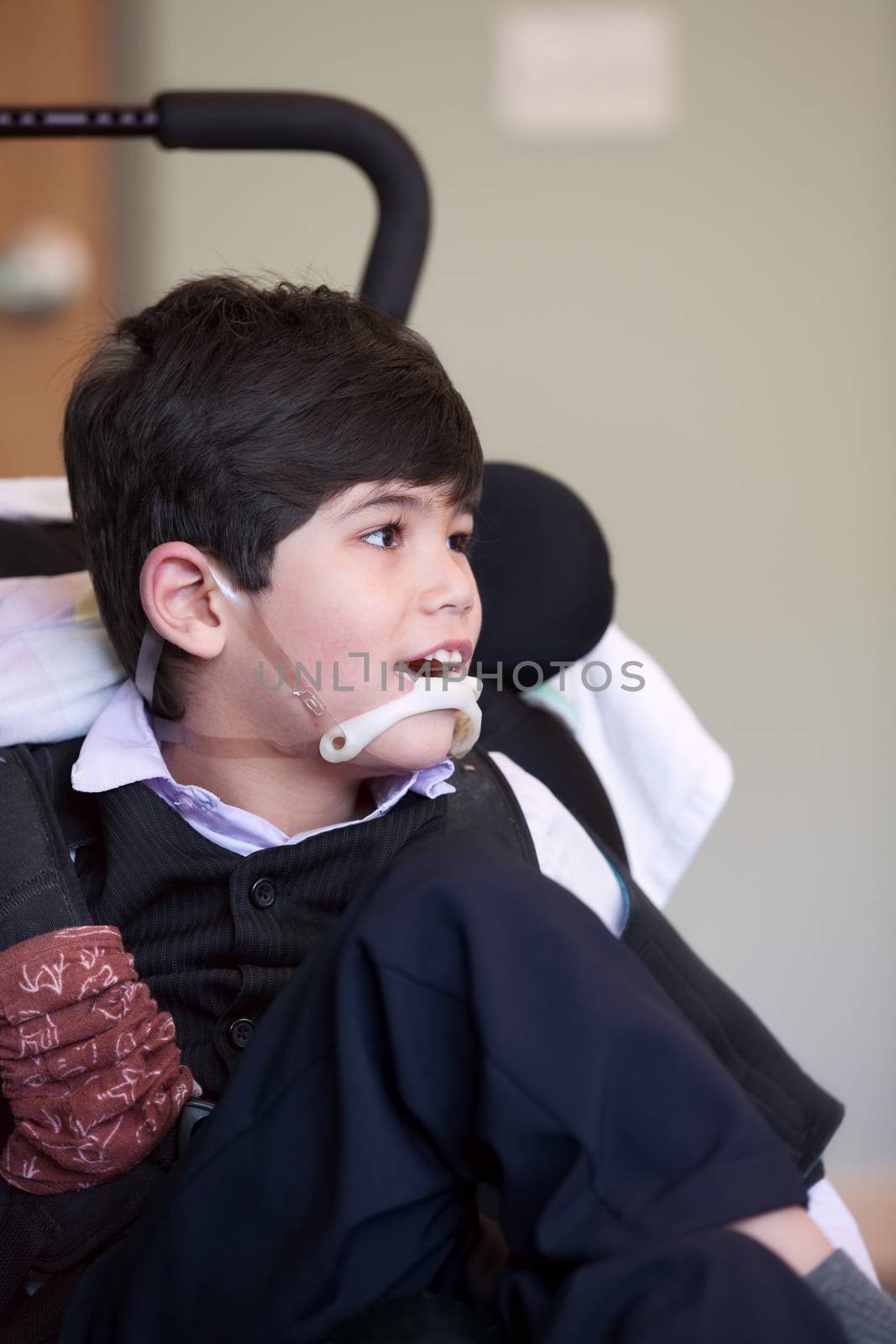 Handsome disabled eight year old biracial boy smiling and relaxing in wheelchair