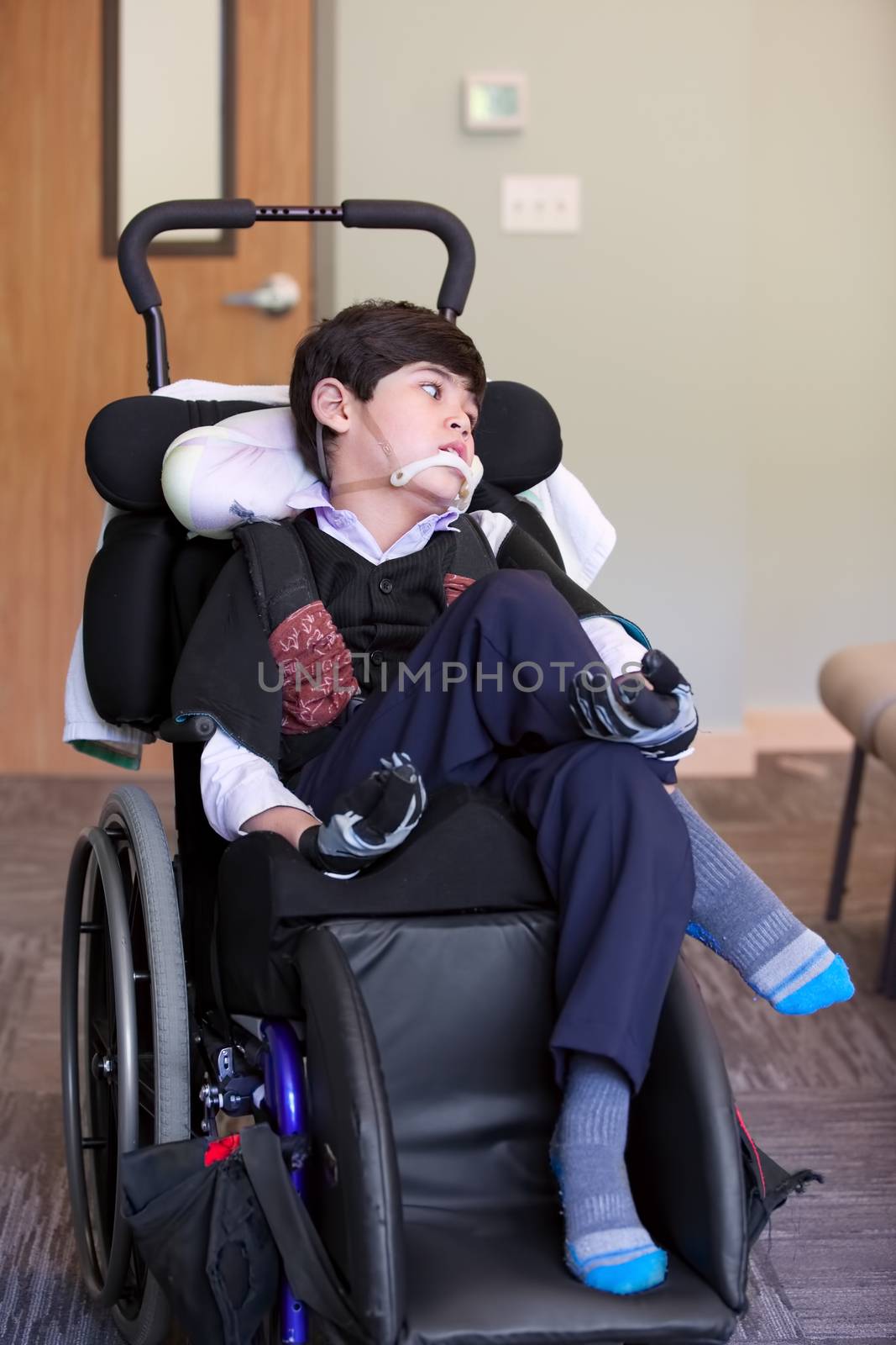 Handsome disabled eight year old biracial boy smiling and relaxing in wheelchair