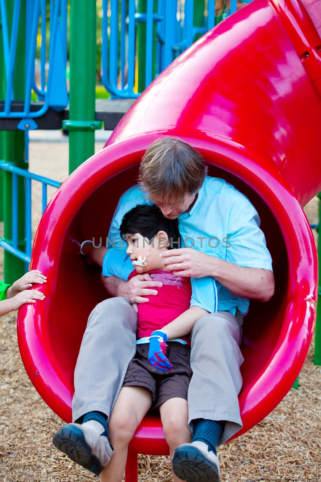 Caucasian father helping disabled son down slide at playground by jarenwicklund