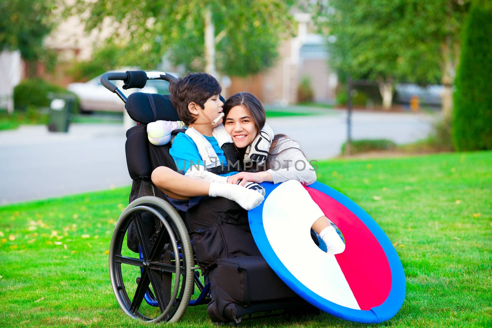 Disabled brother hugging older sister while sitting in wheelchair outdoors by jarenwicklund