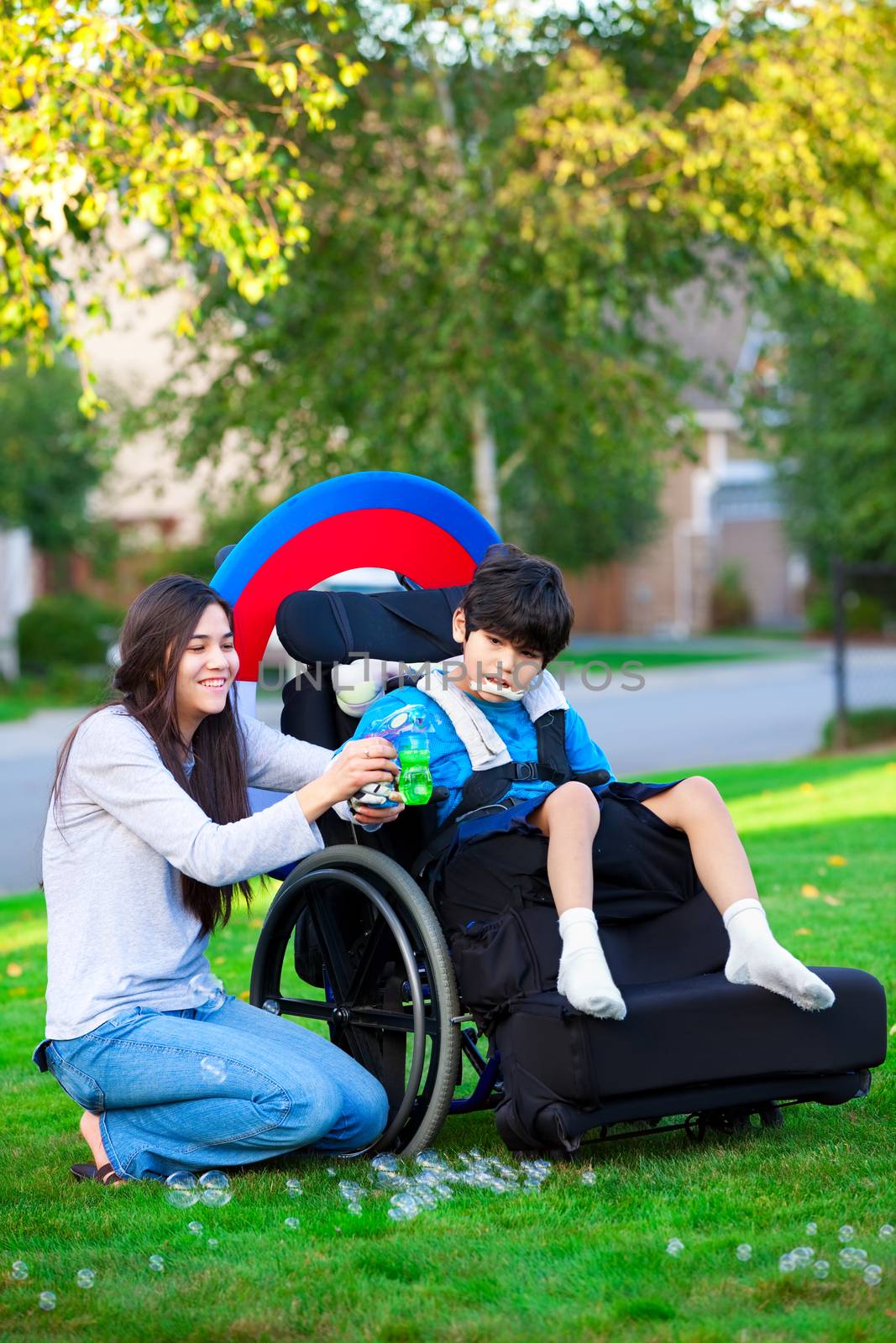 Biracial older sister playing outdoors with disabled little brother in wheelchair