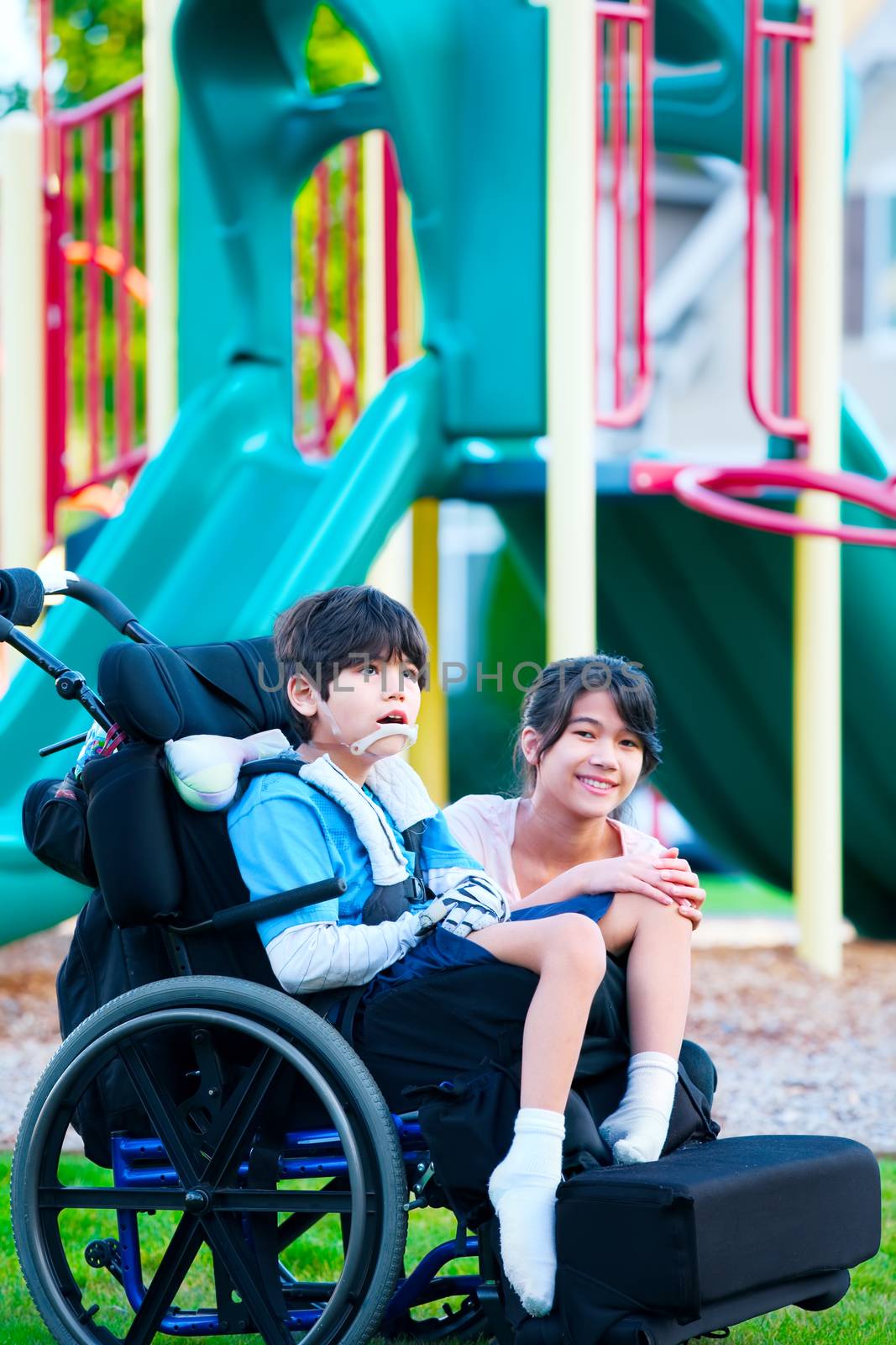 Sister sitting next to disabled brother in wheelchair at playground