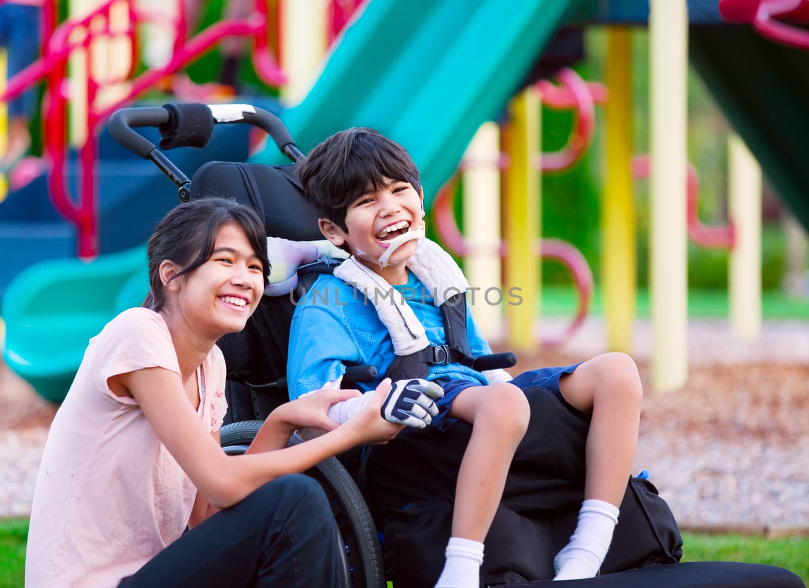 Sister sitting next to disabled brother in wheelchair at playground