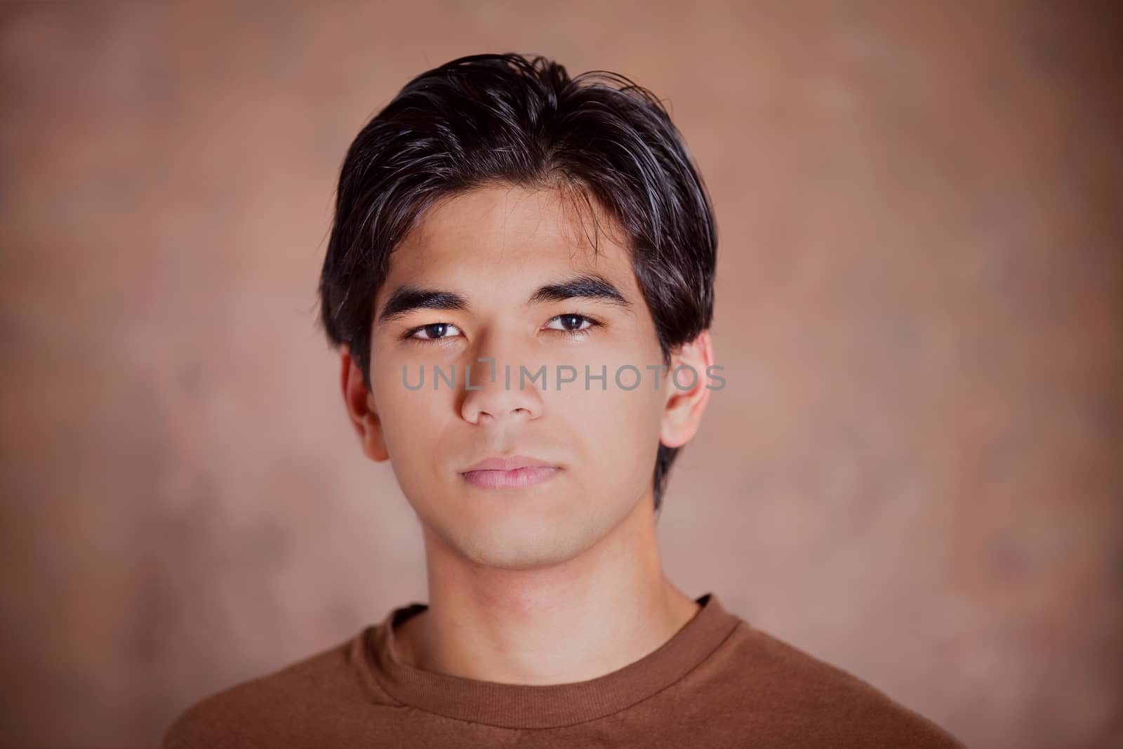 Handsome young man standing against brown background with serious expression