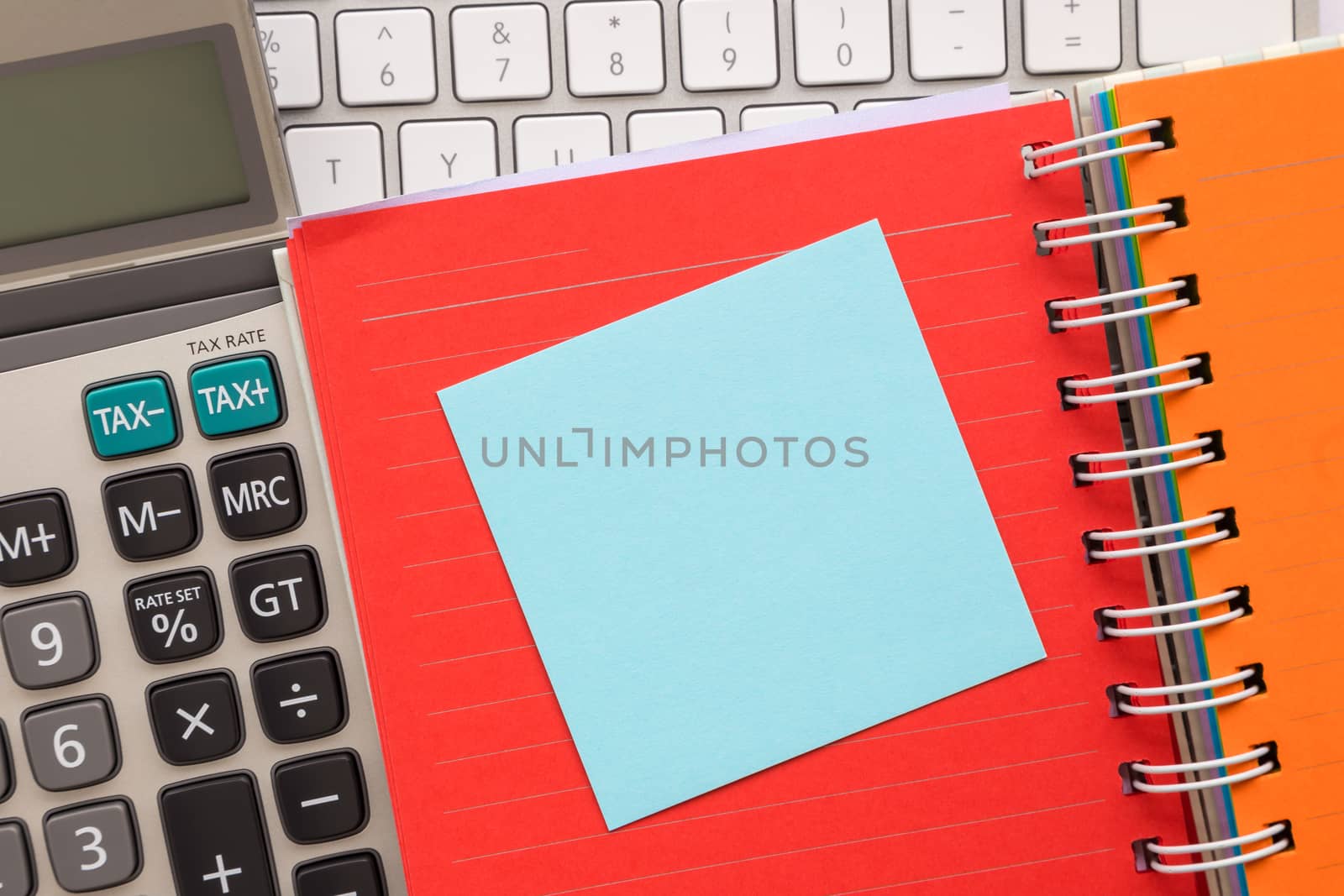 Blue blank notepad on colorful paper book with keyboard and calculator on background